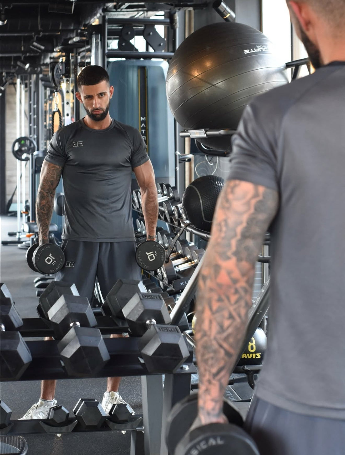 man looking in the gym mirror wearing gym clothes, grey tshirt and shorts working out
