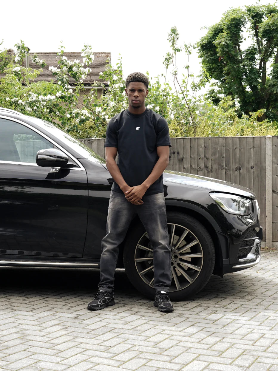 men leaning against a car with black wash jeans and a black tshirt with an E logo in the middle
