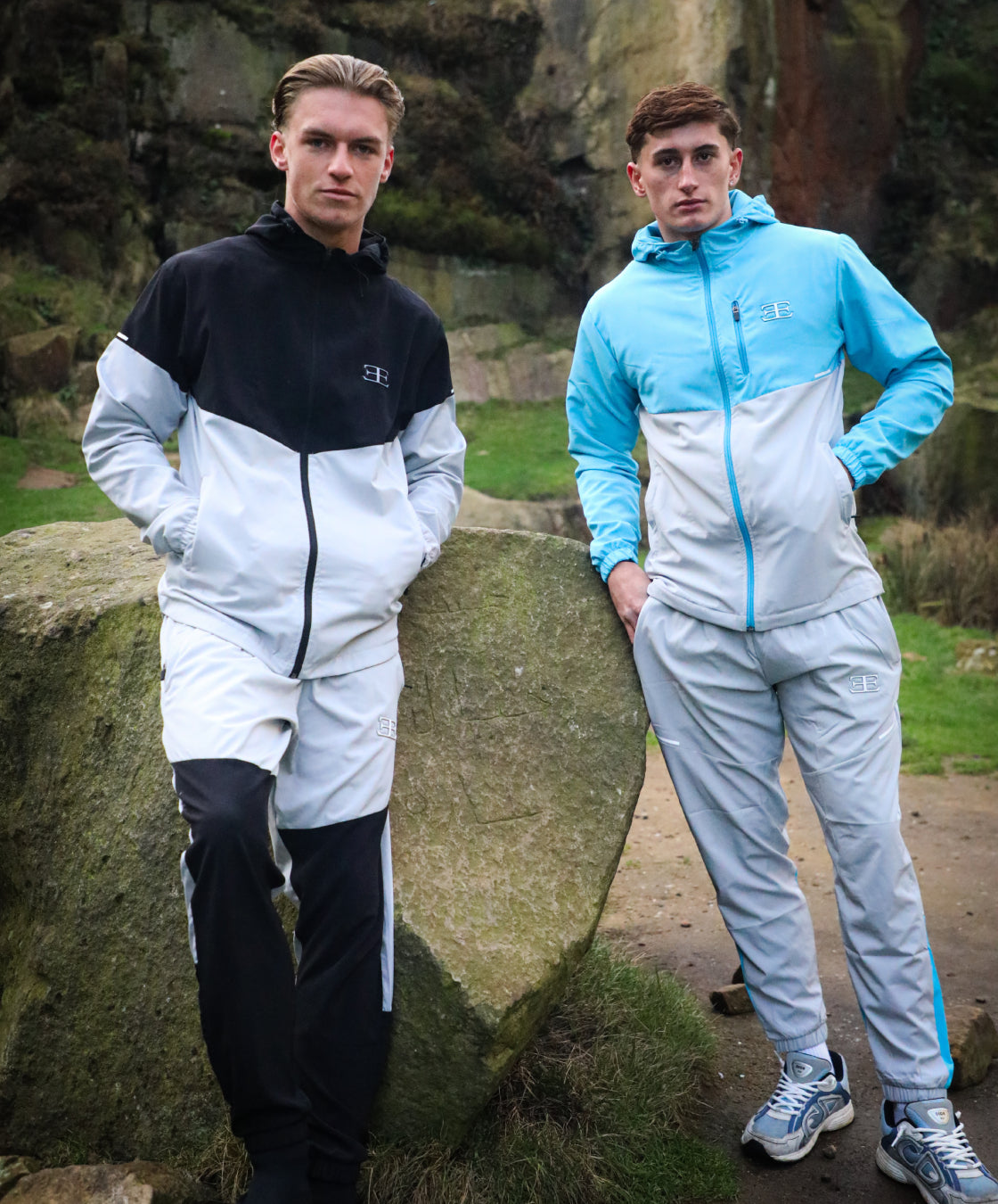 two men wearing tracksuits sets outside, 1 black and grey tracksuit and one wearing sky blue and grey tracksuit