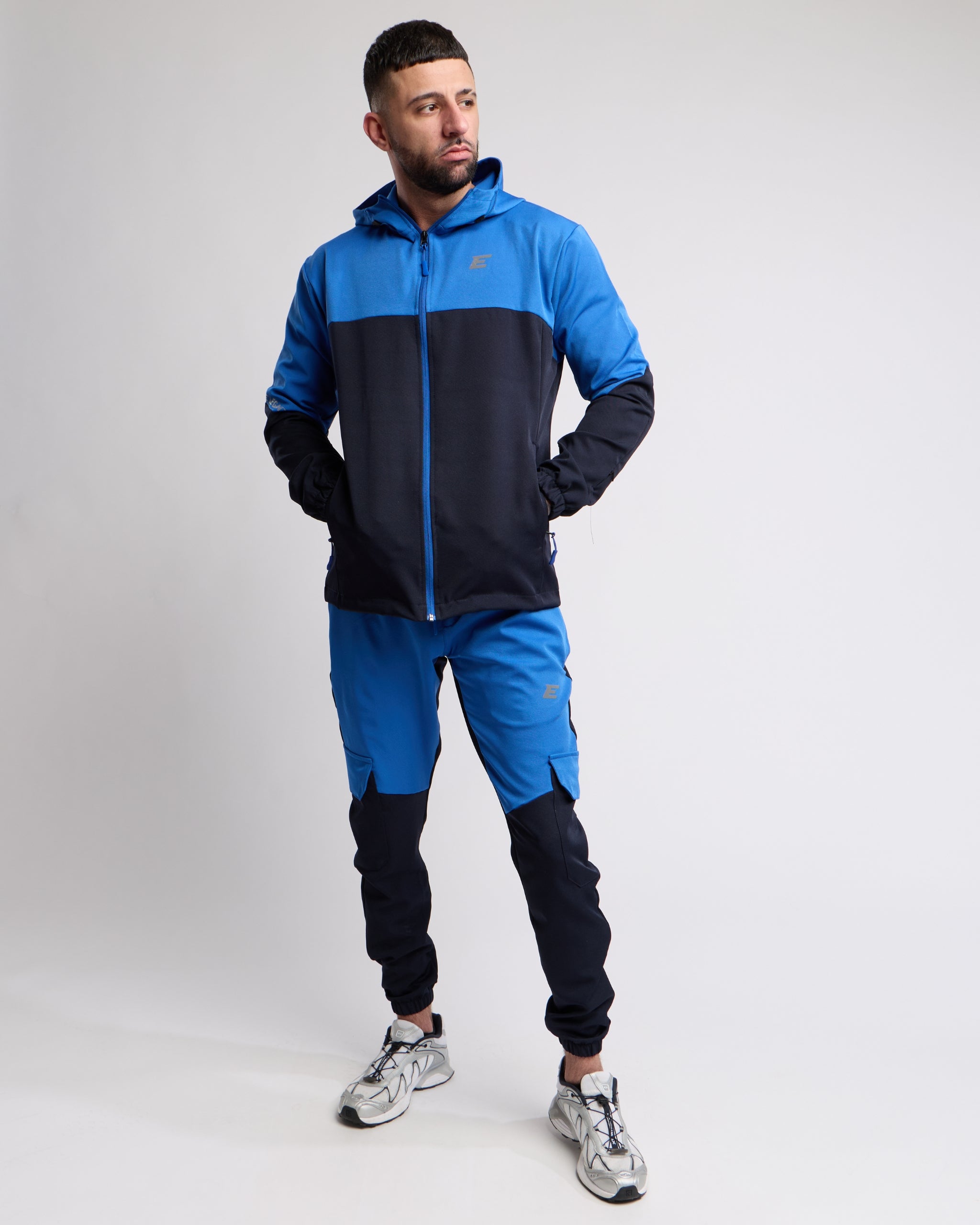 man wearing pink tracksuit jacket with hood up and pink shorts with buildings in background