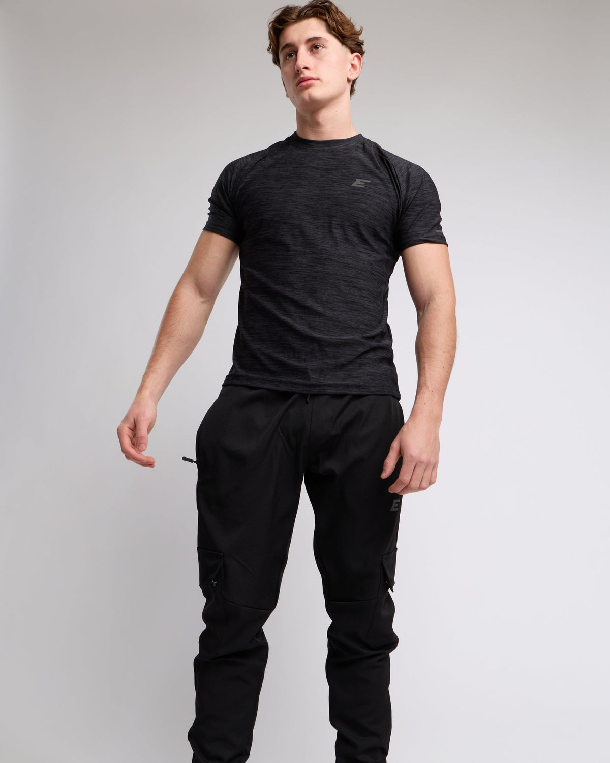 Man wearing a black athletic t-shirt and joggers with a elegante london logo on a light gray background