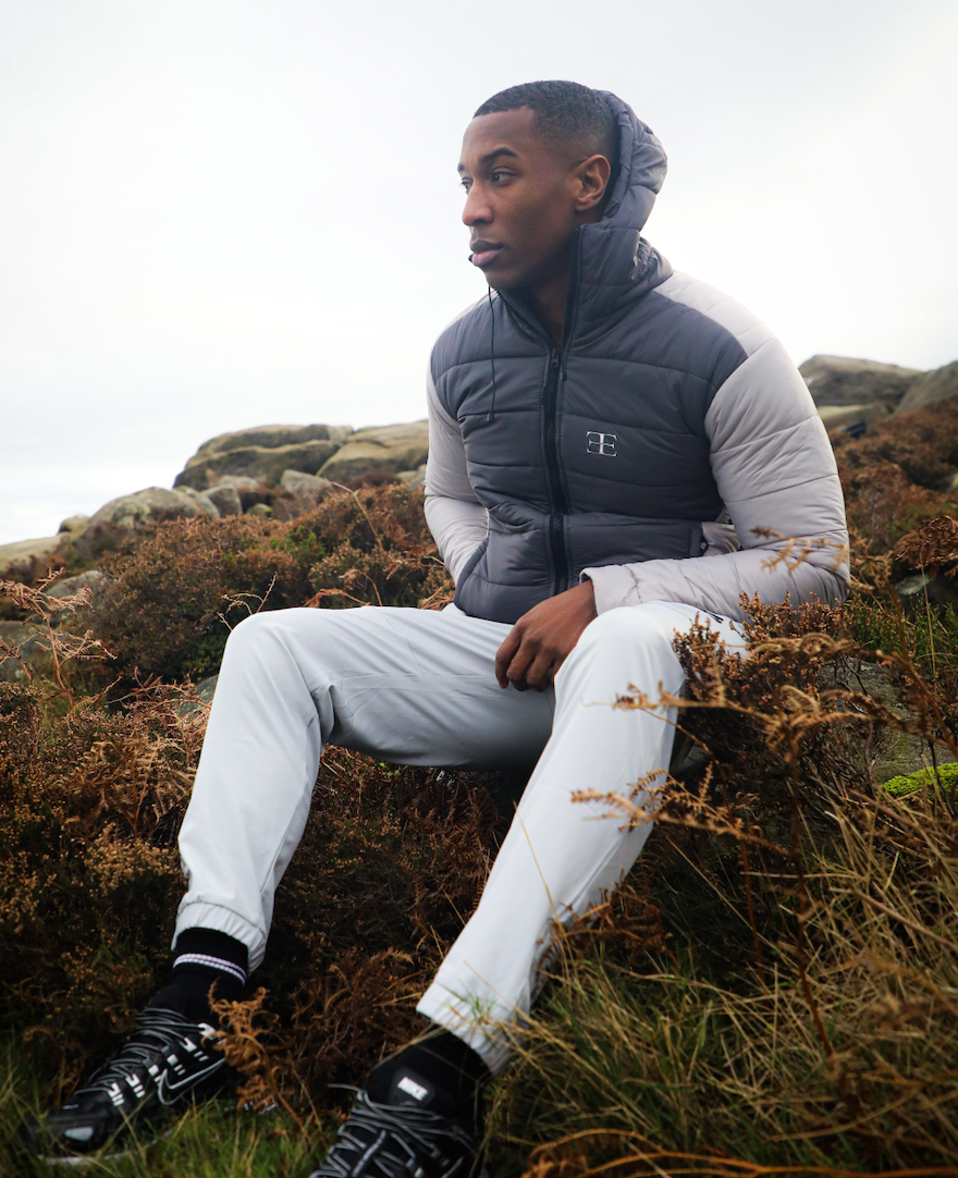 Man wearing grey pants and dark grey and light grey puffer jacket sat on grassy background