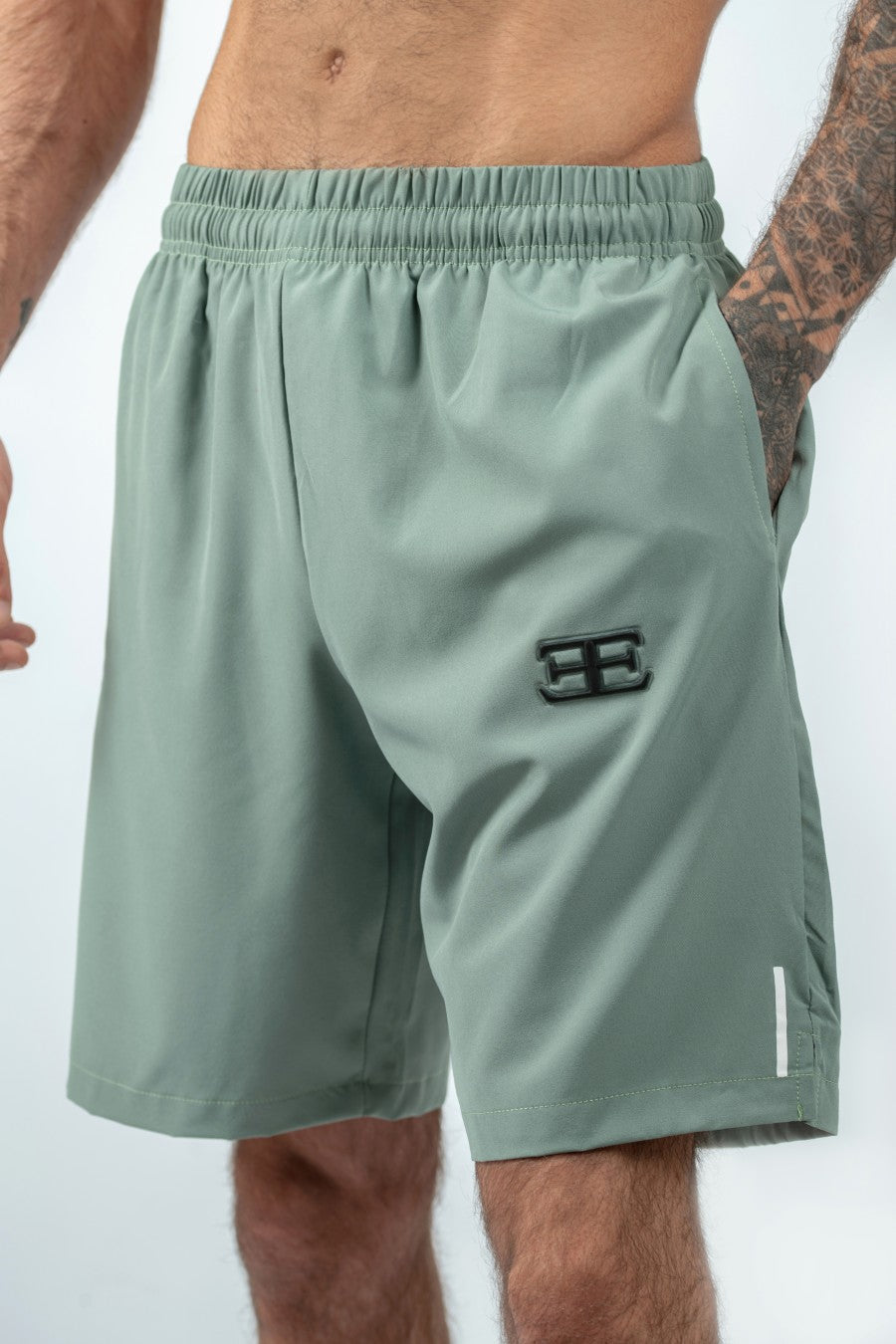 close up of man wearing light green shorts with hand in pocket, with Elegante Clothing badge logo on thigh