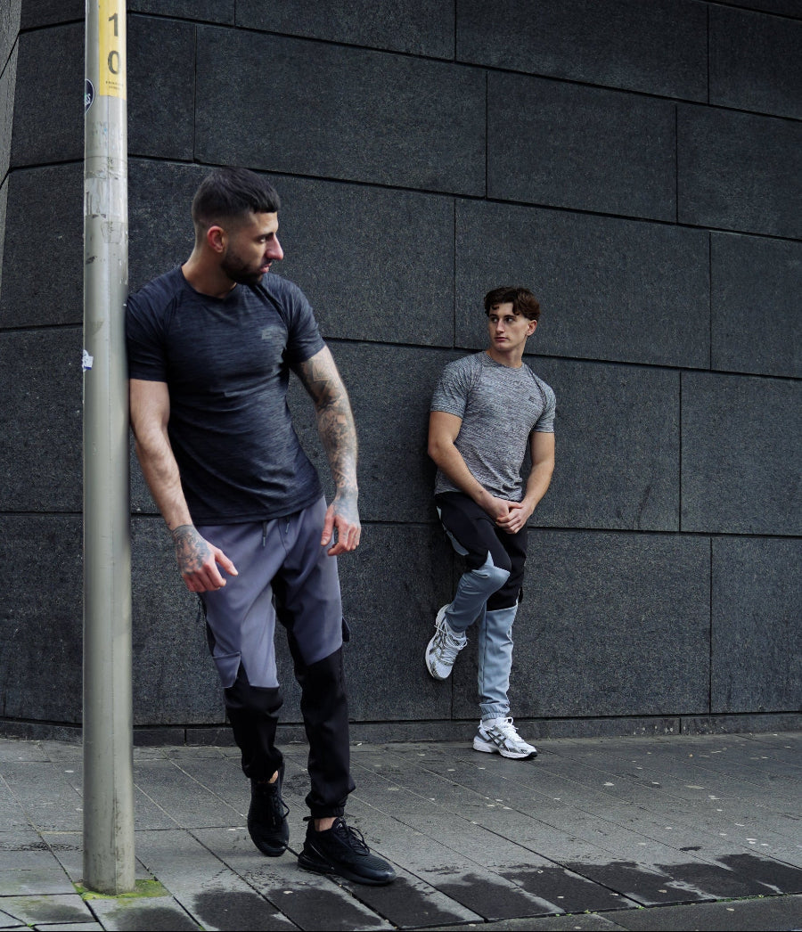 Two men standing on a city street corner wearing athetlic wear with a dark building in the background.