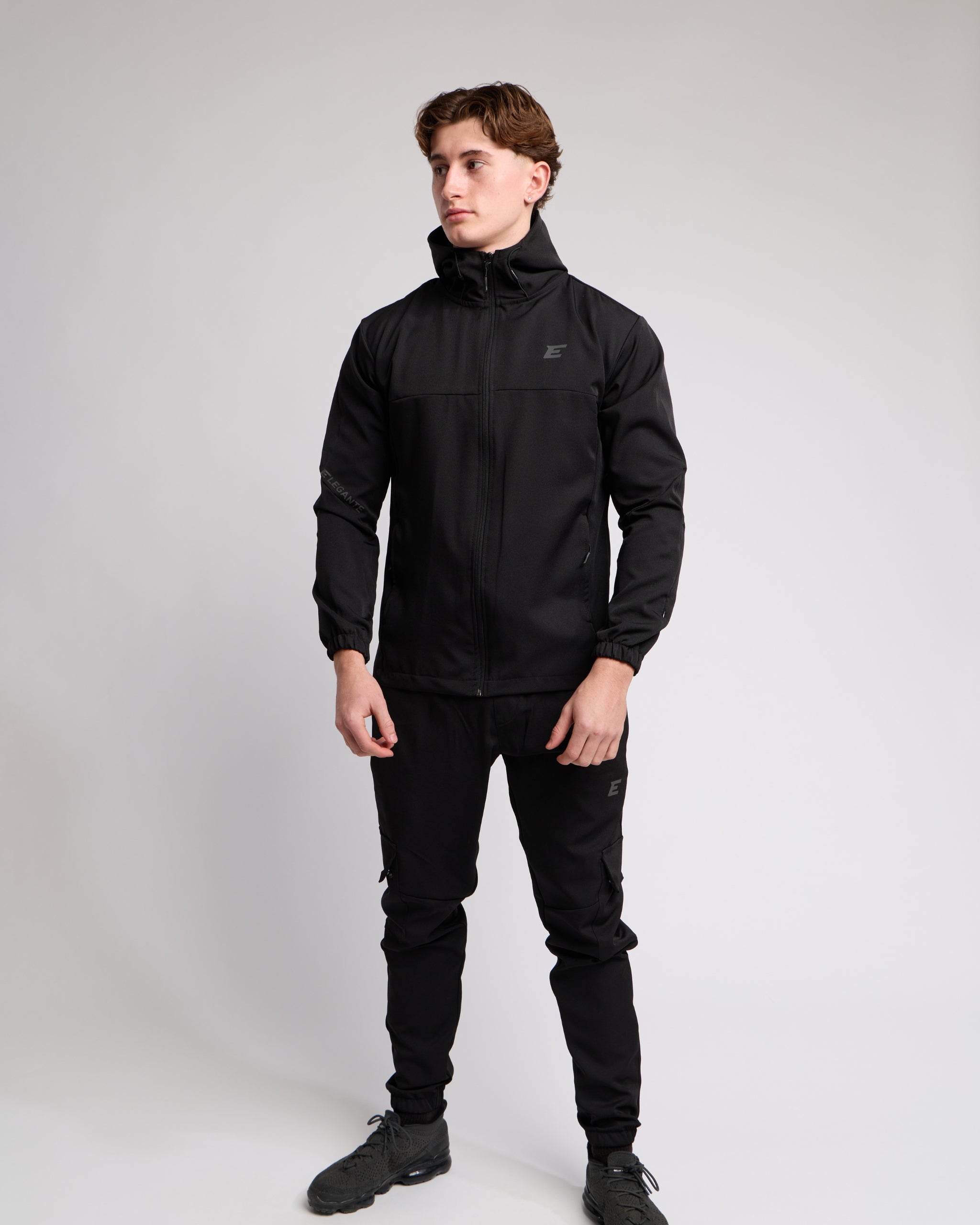 Man wearing an all Black sports tracksuit jacket and trousers on a white background