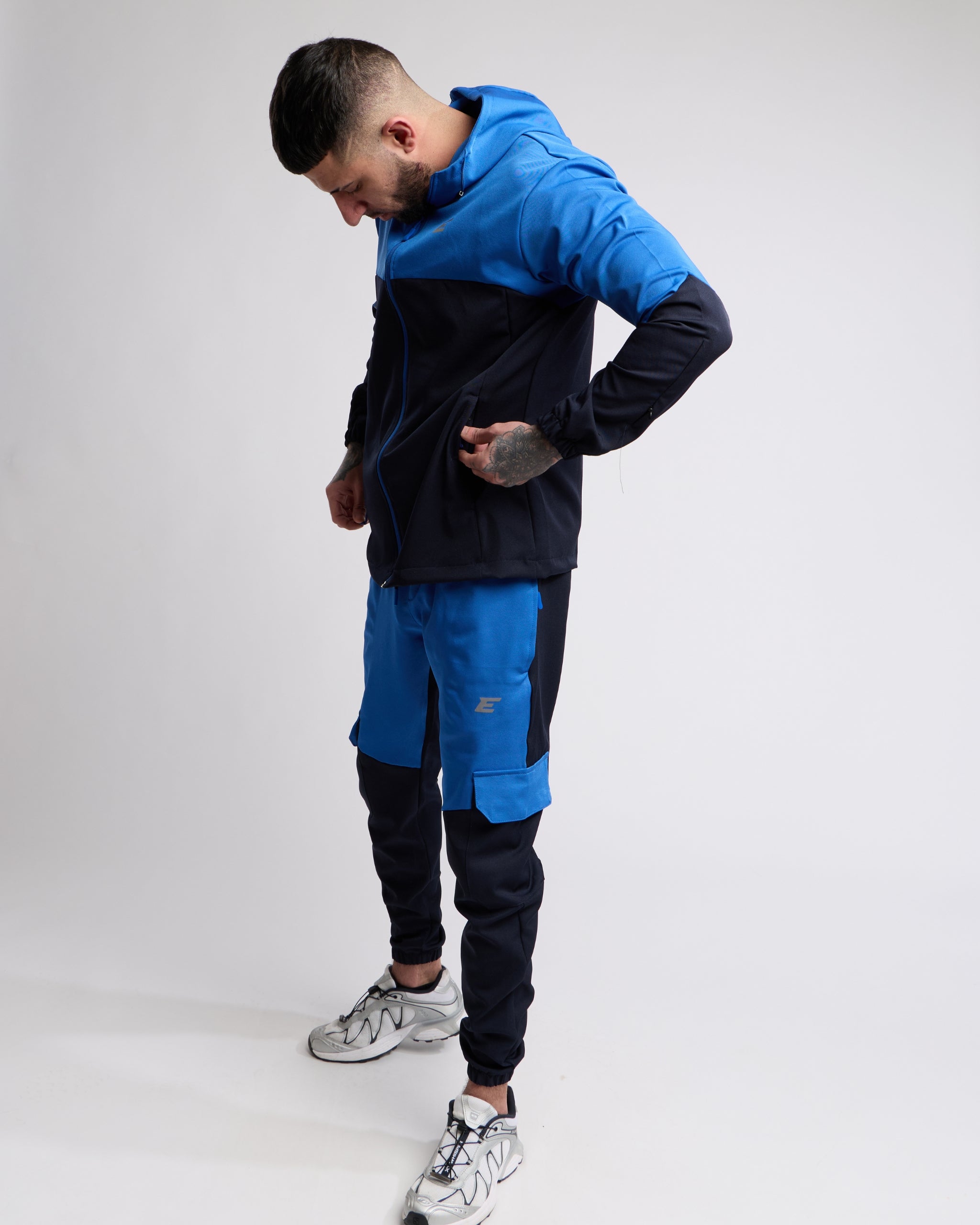 Man wearing a Blue and Navy sports tracksuit jacket with matching tracksuit pants on a white background