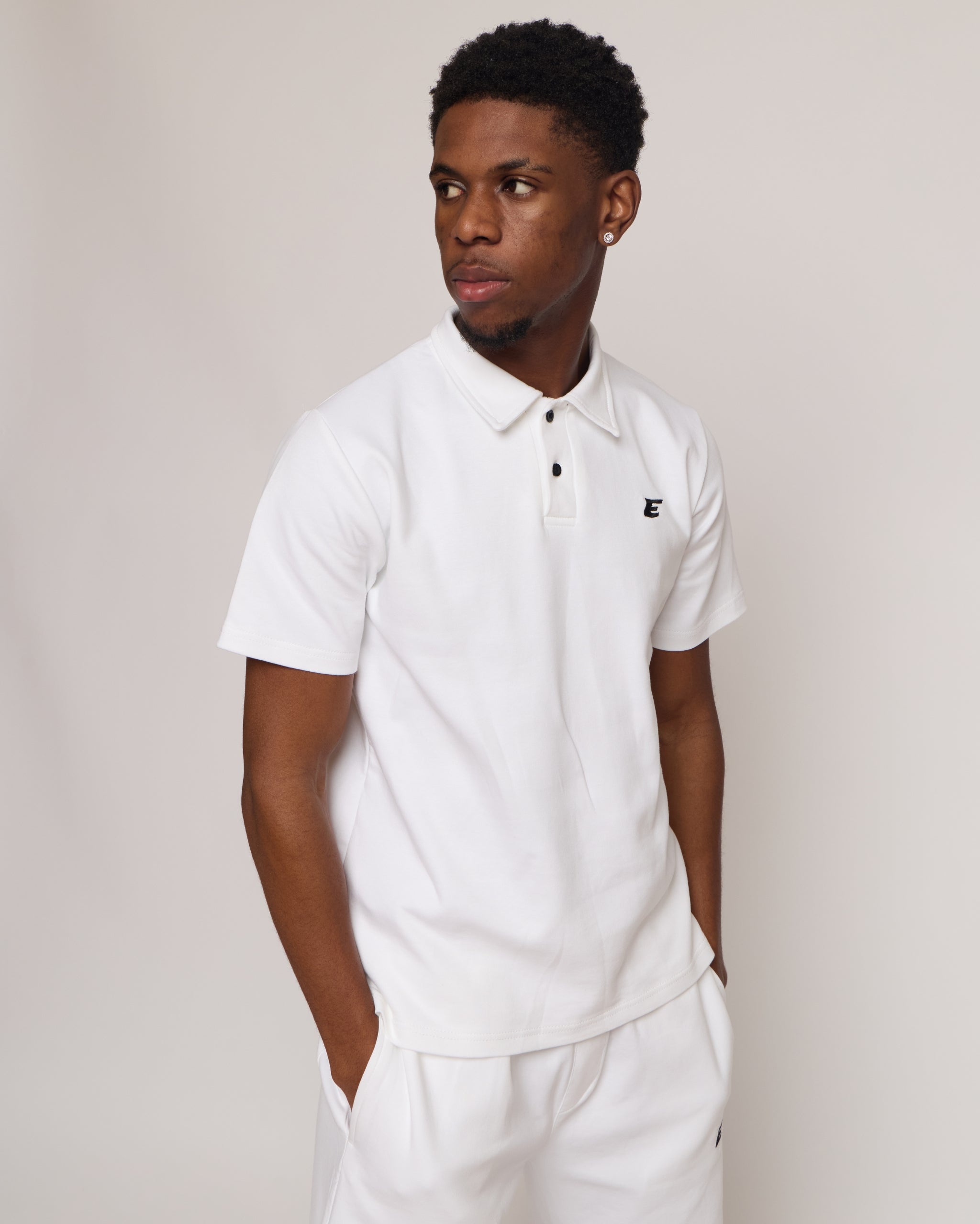 Man wearing a white polo shirt and shorts with an 'E' logo, standing against a plain background