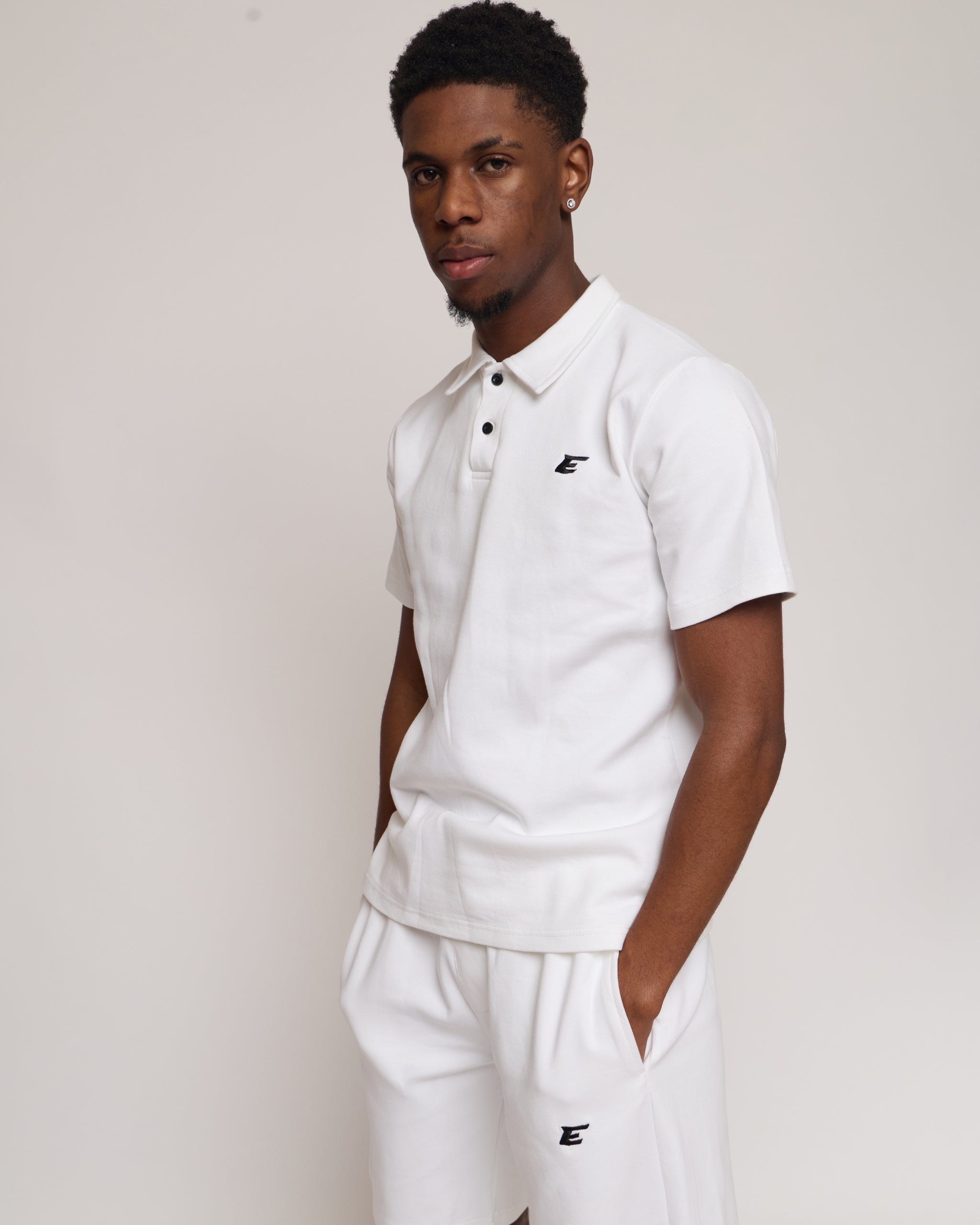 Man wearing a white polo shirt and shorts with an 'E' logo, standing against a plain background