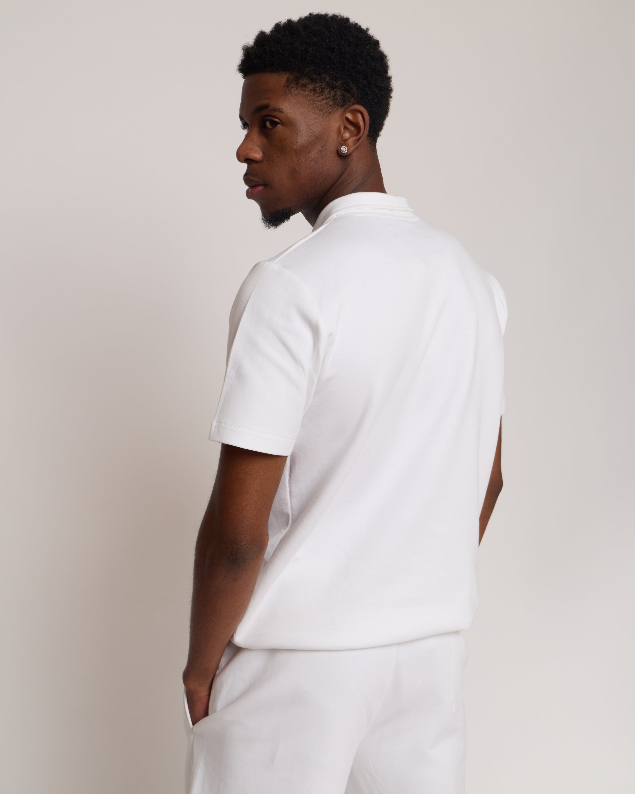 Man wearing a white polo shirt and shorts, standing against a plain background