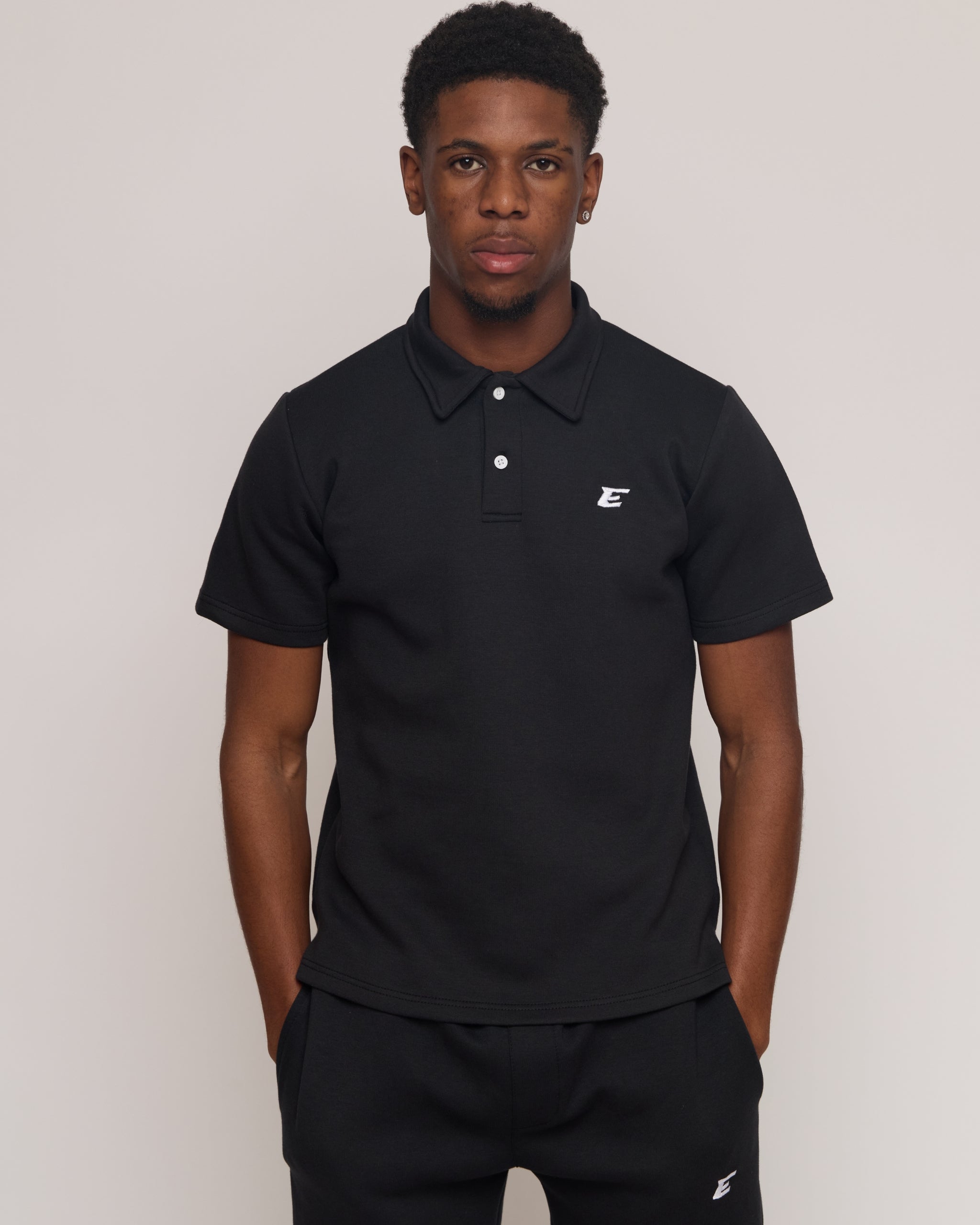 Man wearing a black polo shirt and shorts with an 'E' logo, standing against a plain background