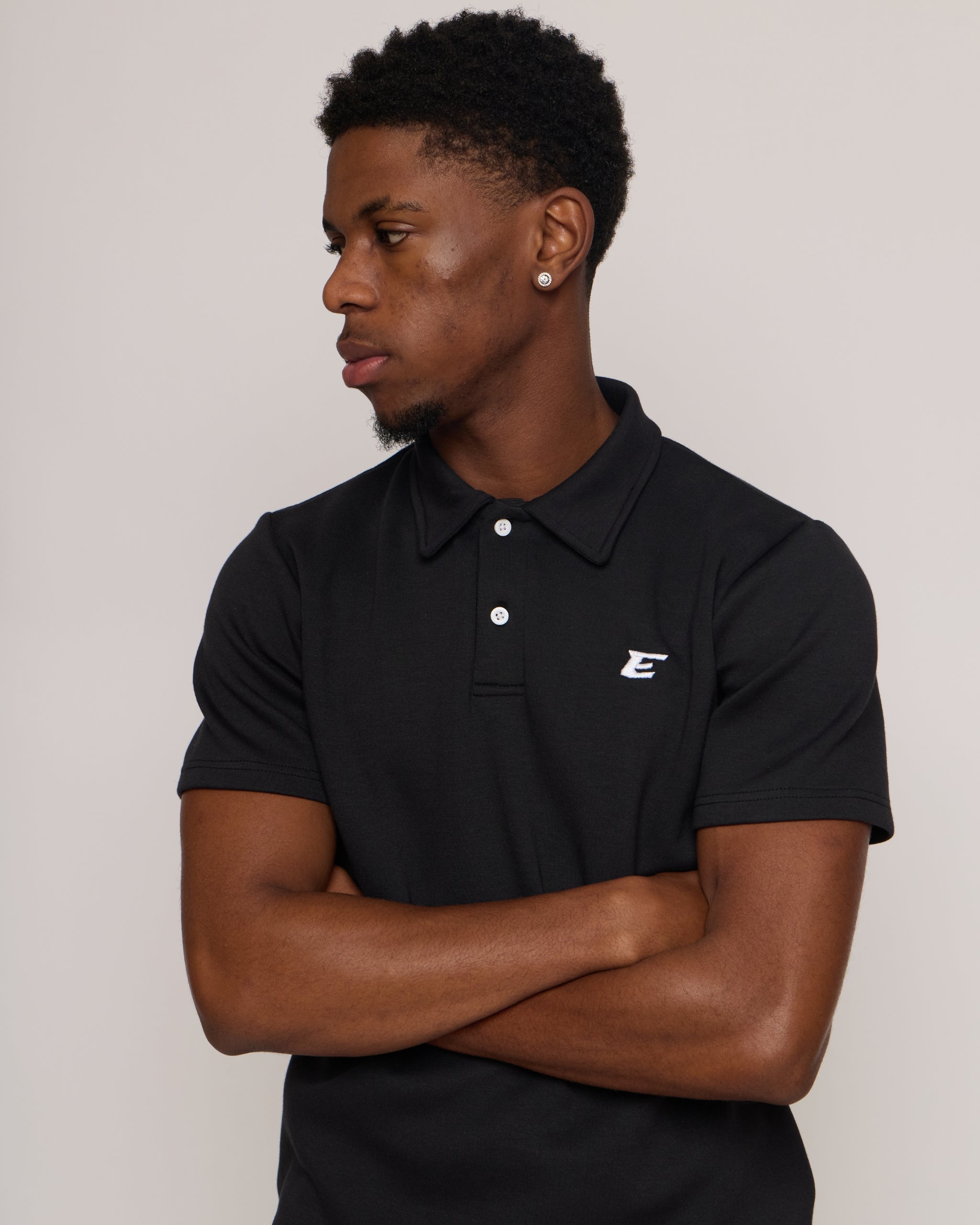 Man wearing a black polo shirt and shorts with an 'E' logo, standing against a plain background