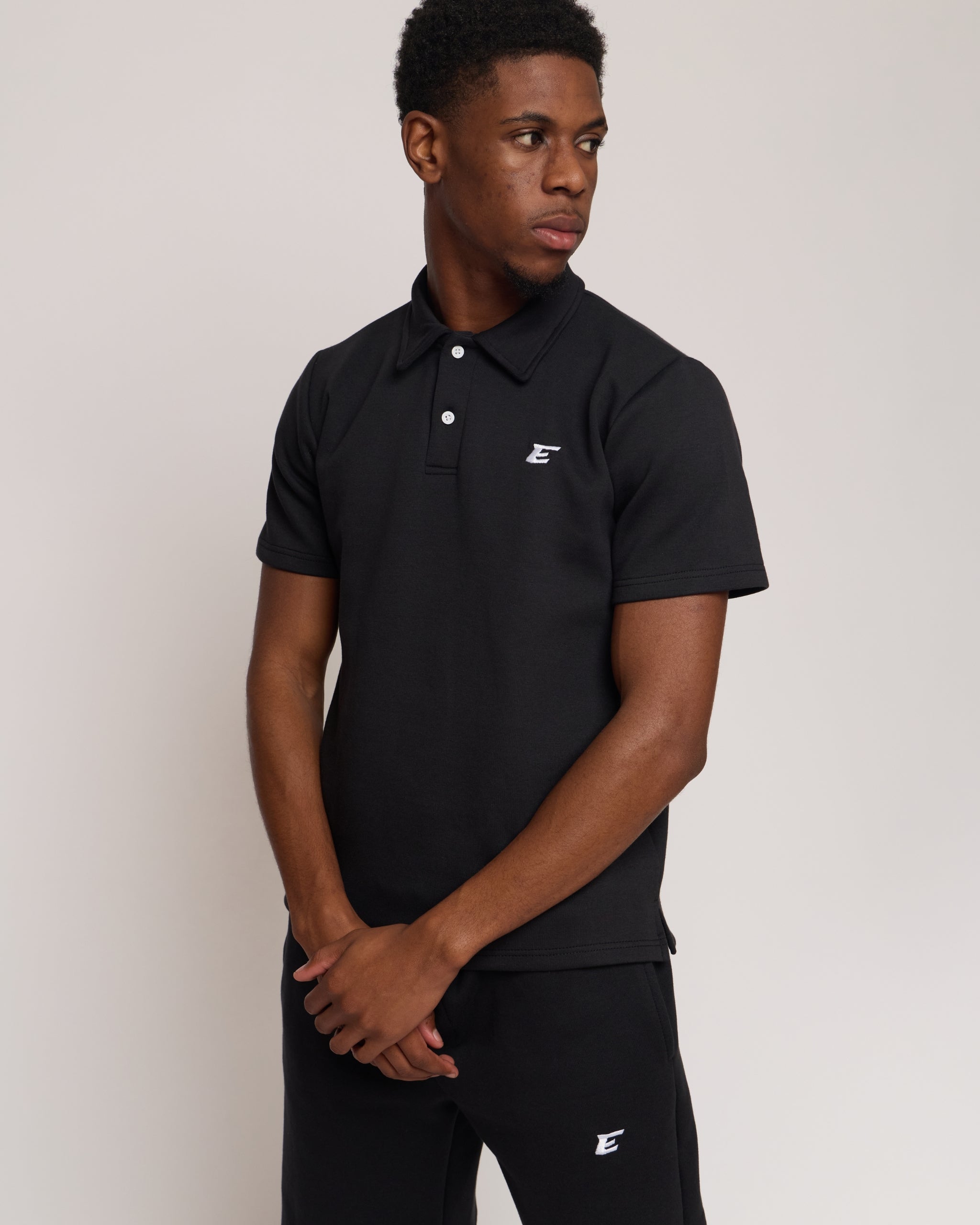 Man wearing a black polo shirt and shorts with 'E' brand logo on a white background