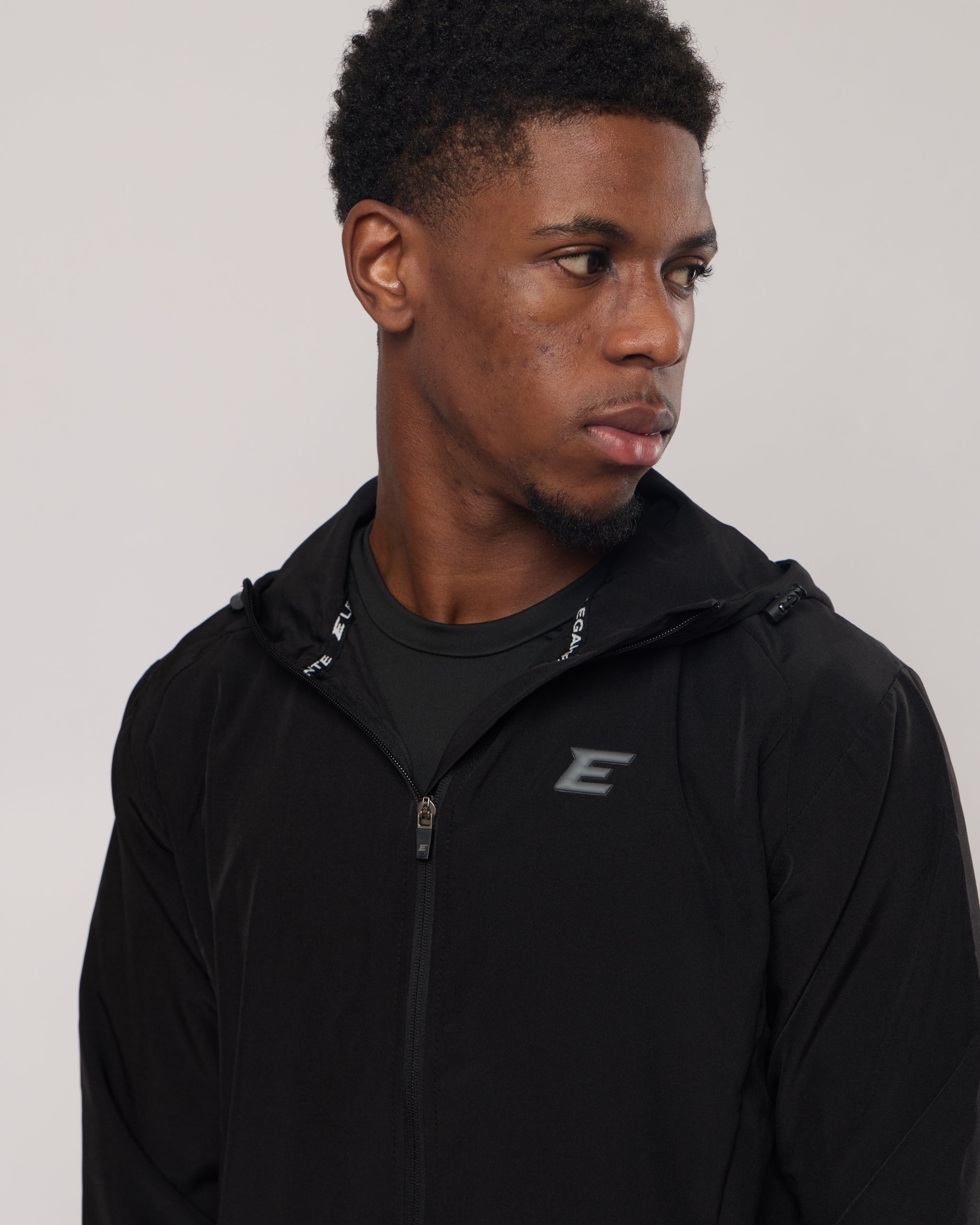 Man wearing a black jacket with a logo on a plain background