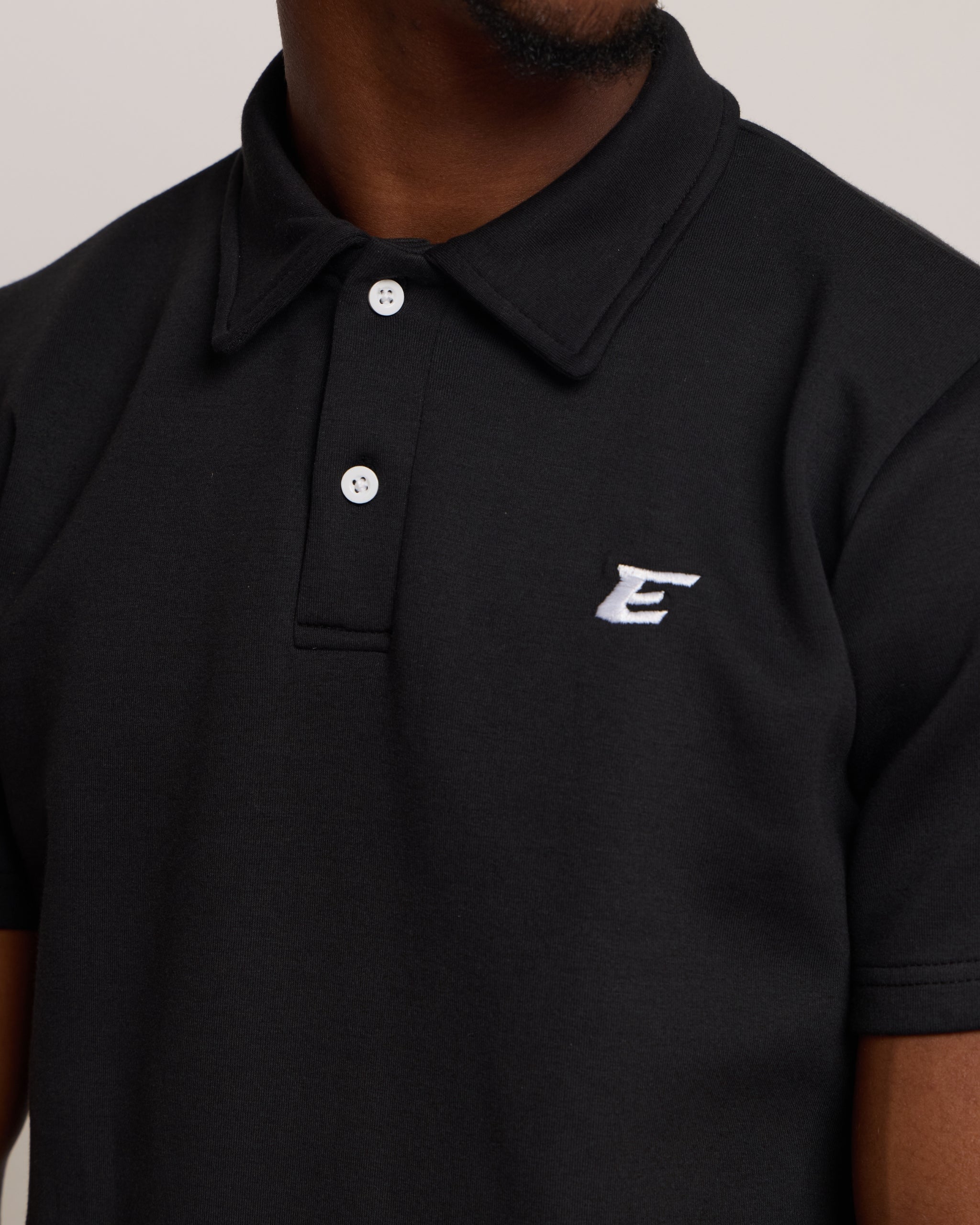 Black polo shirt with an 'E' logo on a neutral background