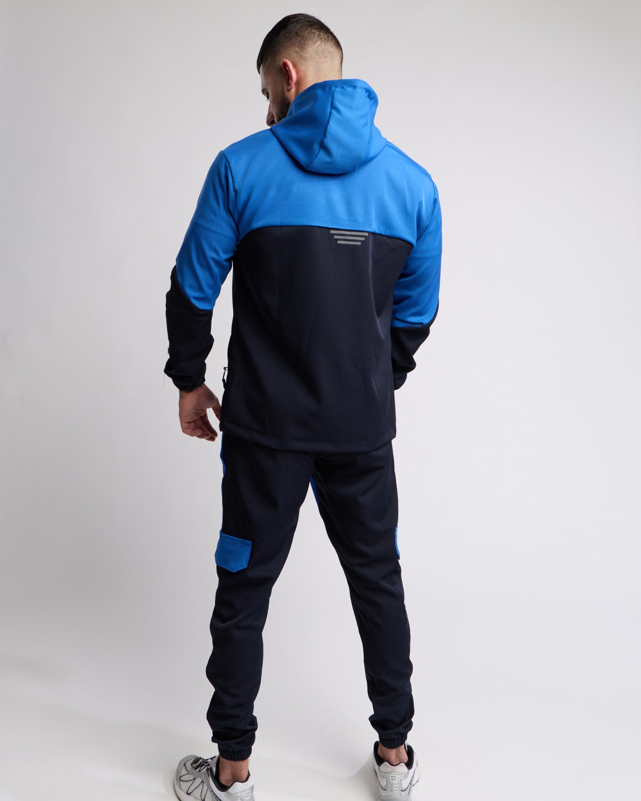 Man wearing a Blue and Navy sports tracksuit jacket with matching tracksuit pants on a white background