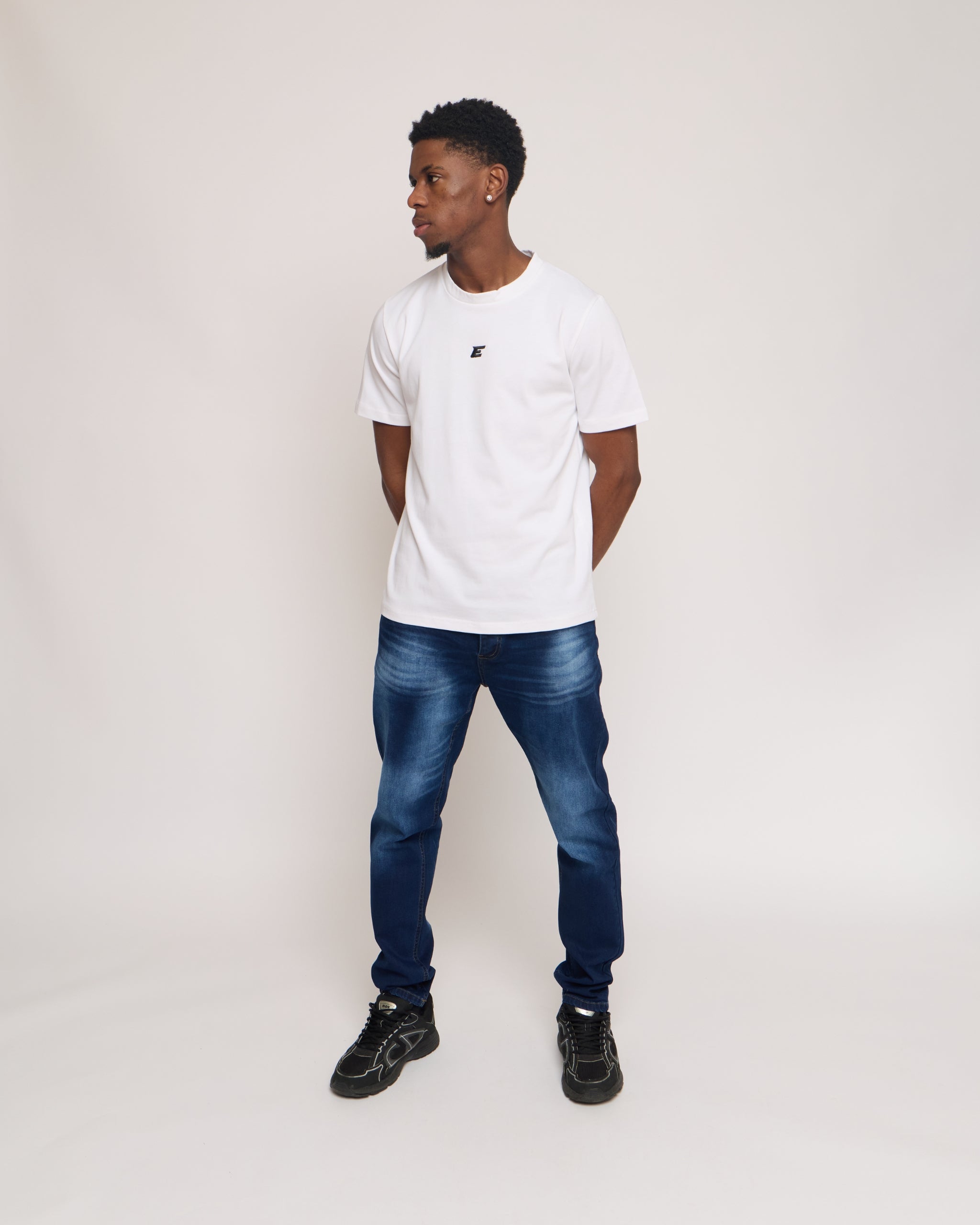 man wearing a white cotton t-shirt with black 'E' Logo and blue denim jeans on a white background