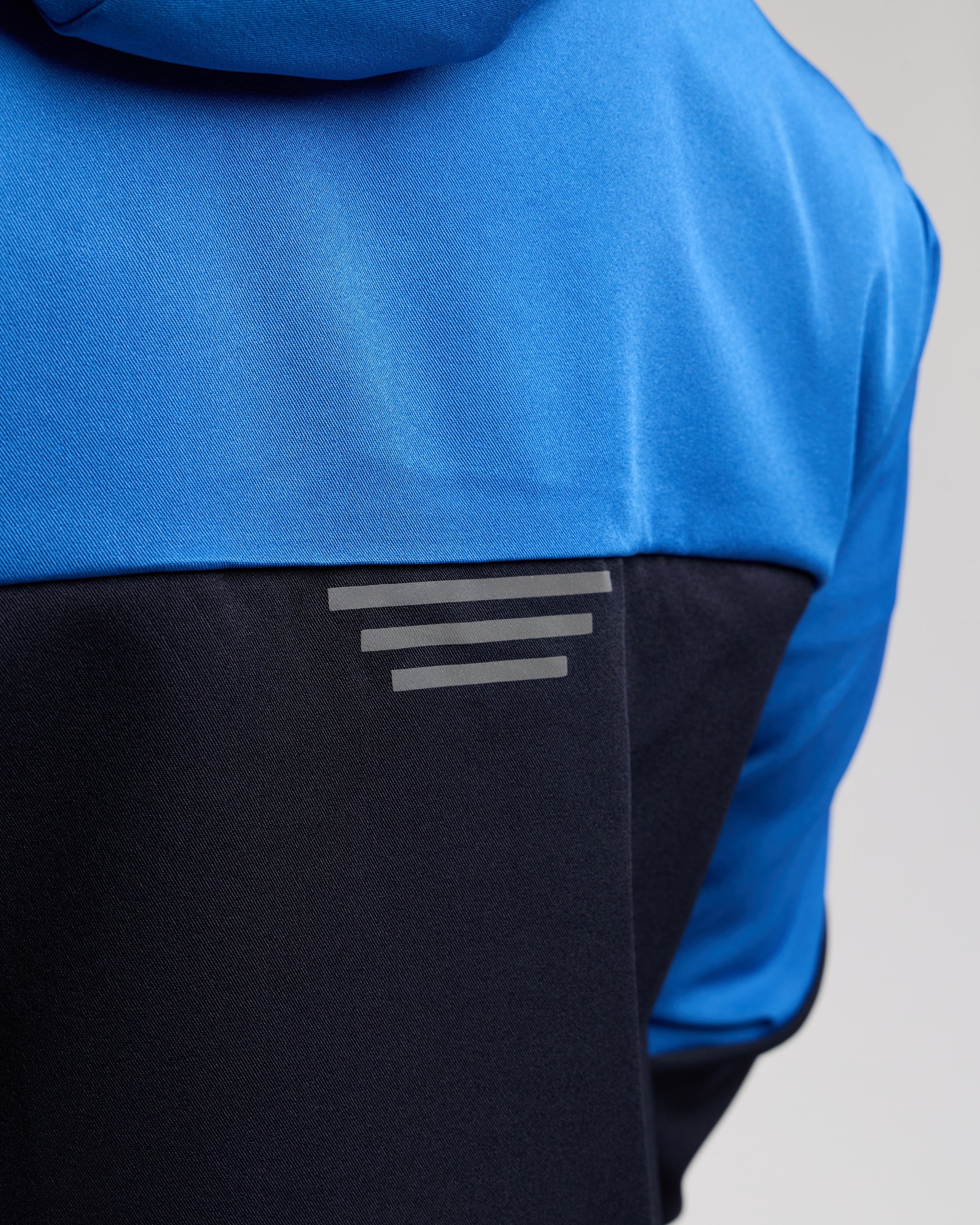 Blue and black jacket with a reflective ascent on a light gray background