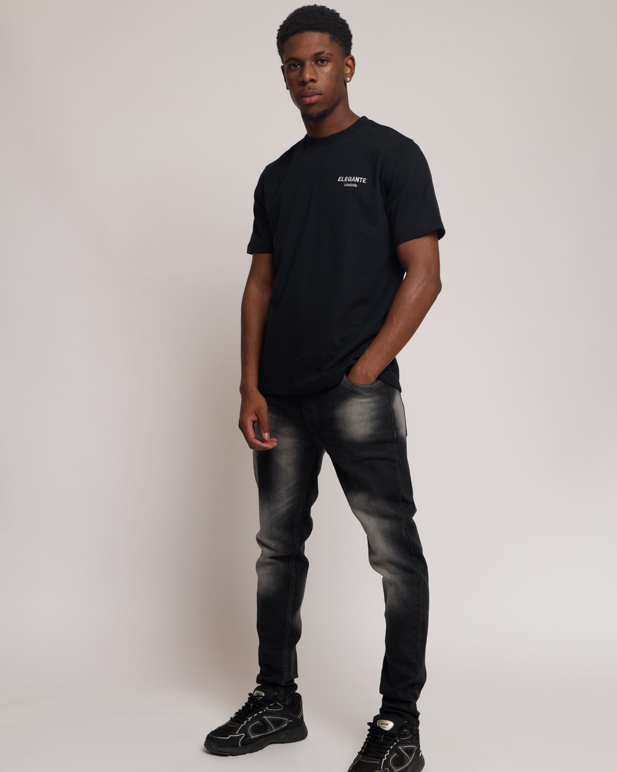 man wearing a black cotton t-shirt with elegante logo and black jeans against a plain background