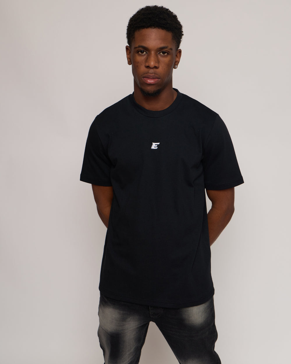 man wearing a black cotton t-shirt with 'E' Logo and jeans on a white background