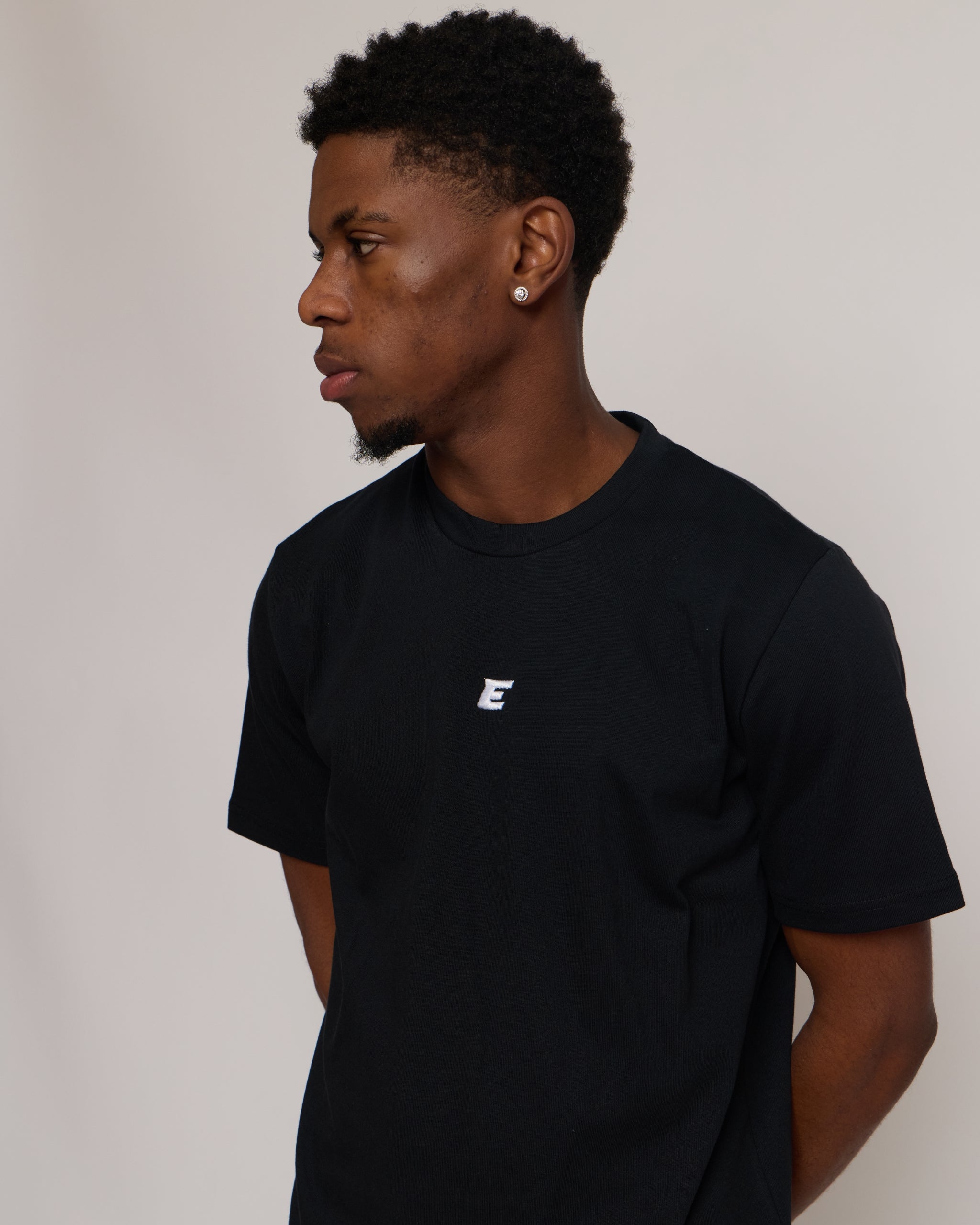 Man wearing a black t-shirt with a small white 'E' logo on a plain background