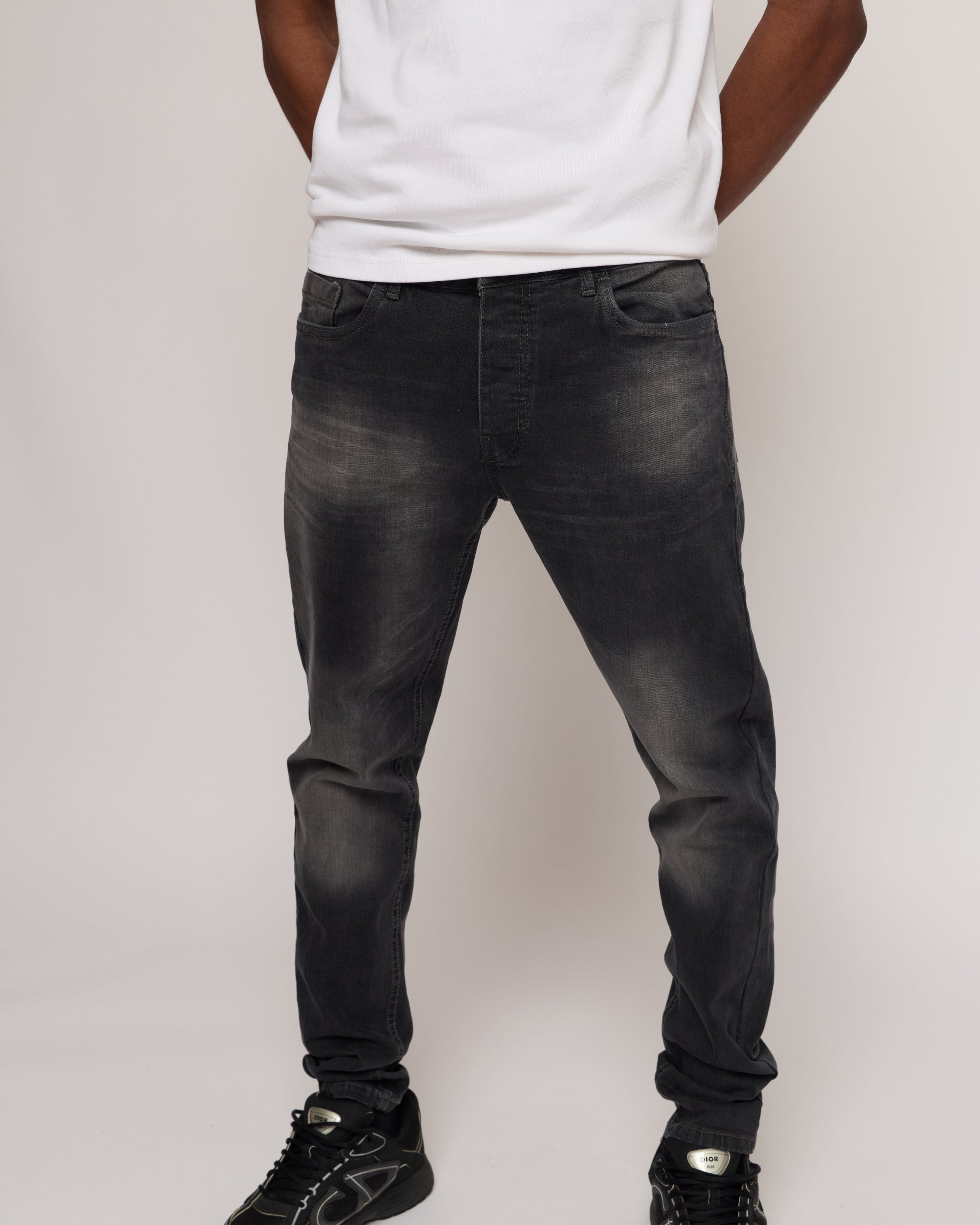 man wearing black distressed jeans and a white shirt on a plain background
