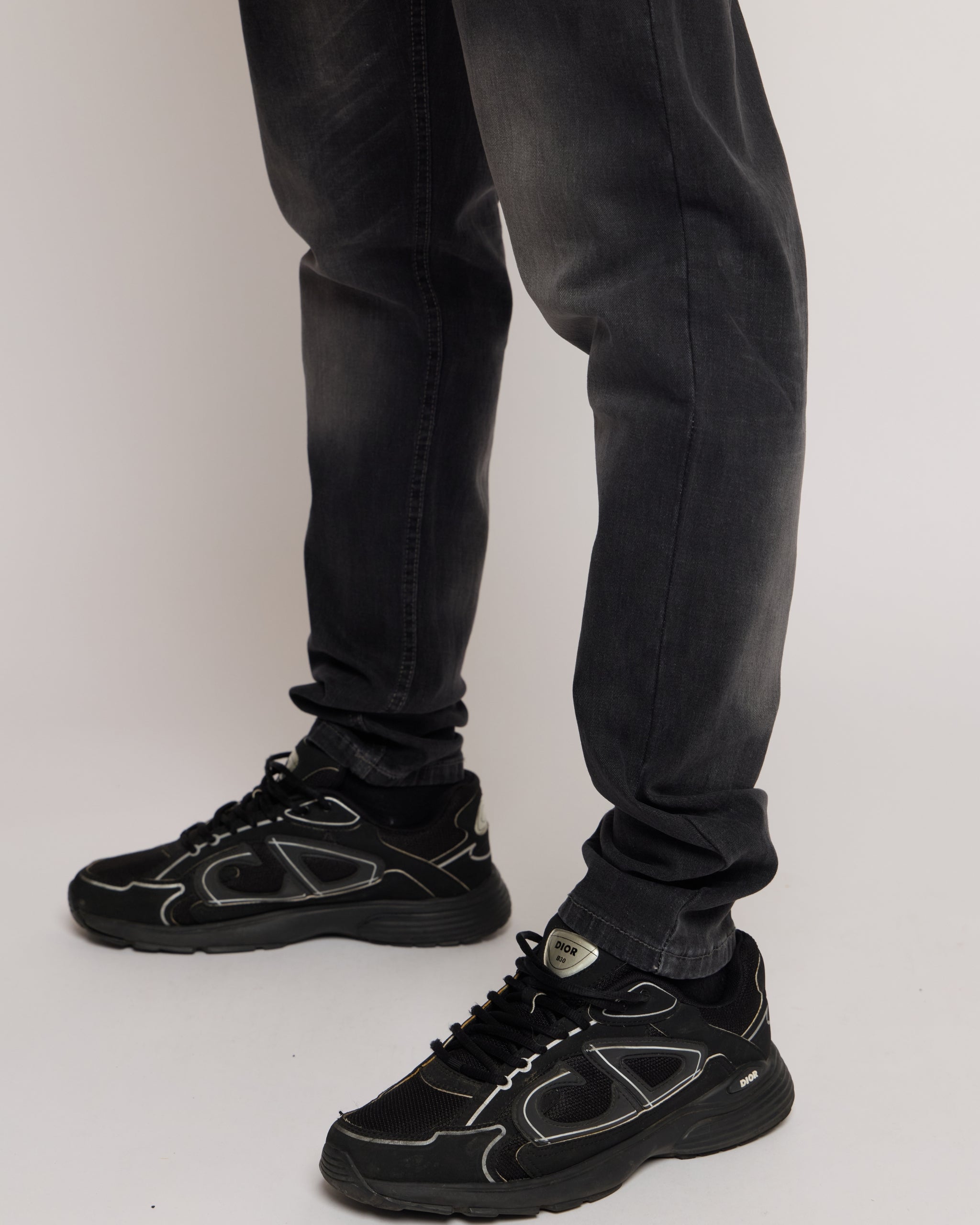 Person wearing black sneakers and grey jeans on a white background