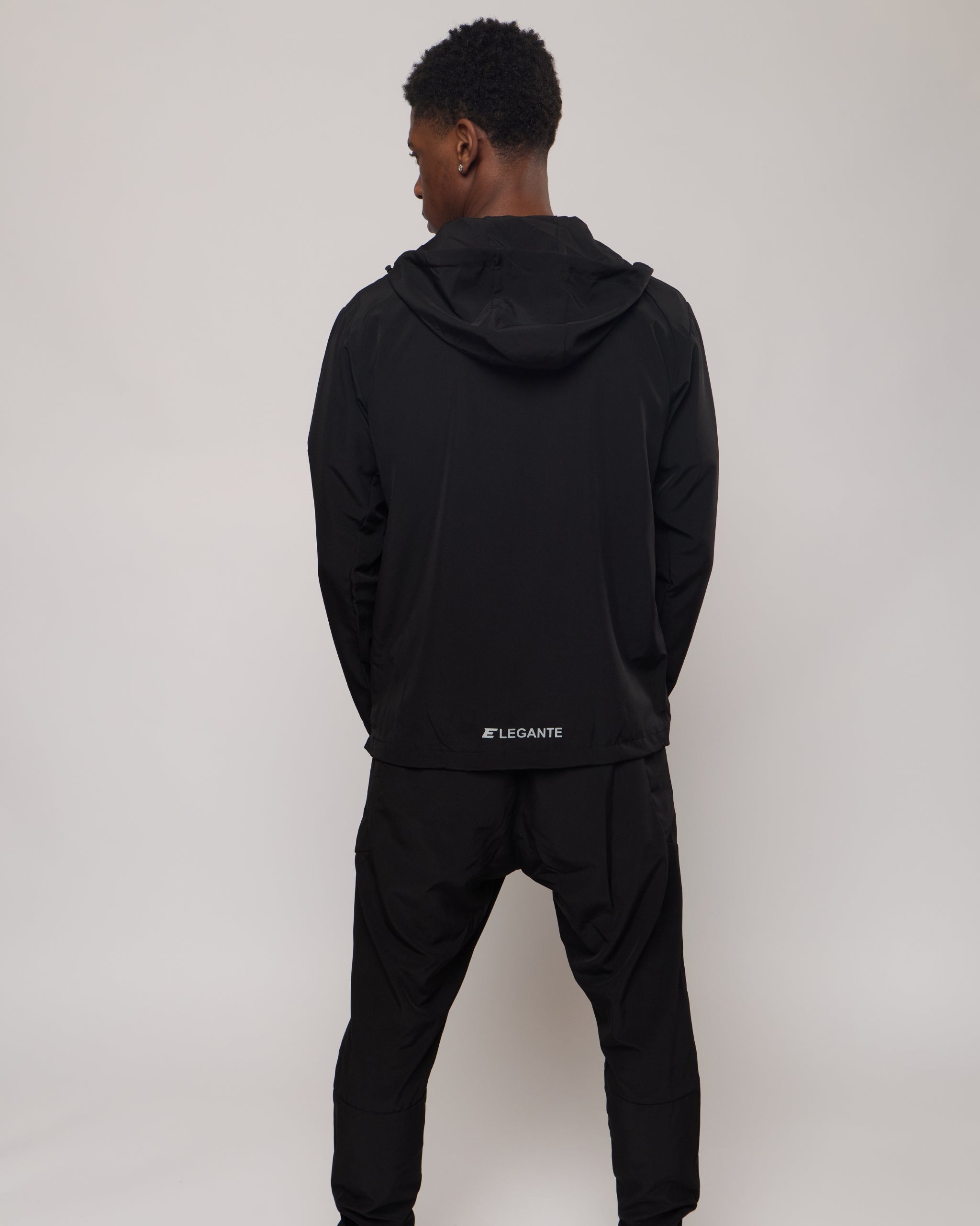 man wearing a black tracksuit jacket with hood and tracksuit pants on a white background