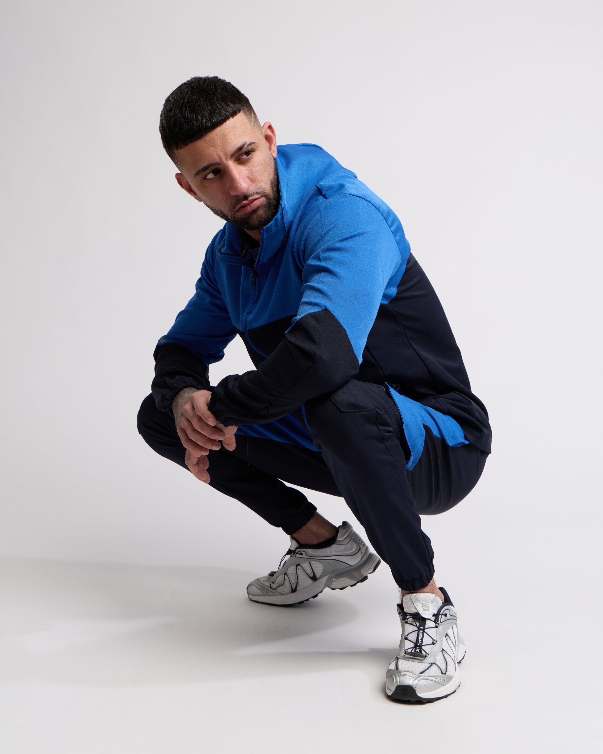 Man wearing a Blue and Navy sports tracksuit jacket with matching tracksuit pants on a white background