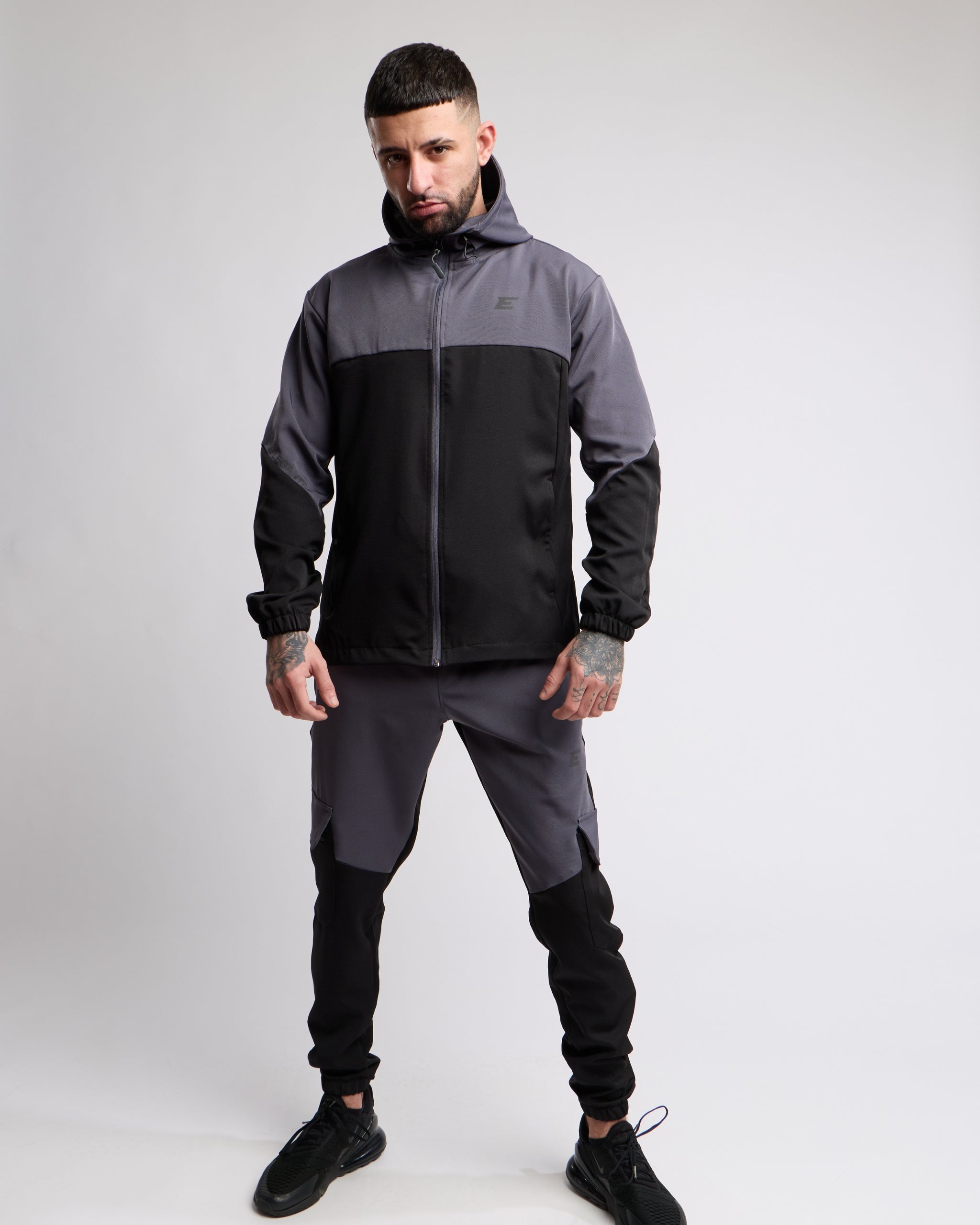 Man wearing a black and gray sports tracksuit jacket with matching tracksuit pants on a white background