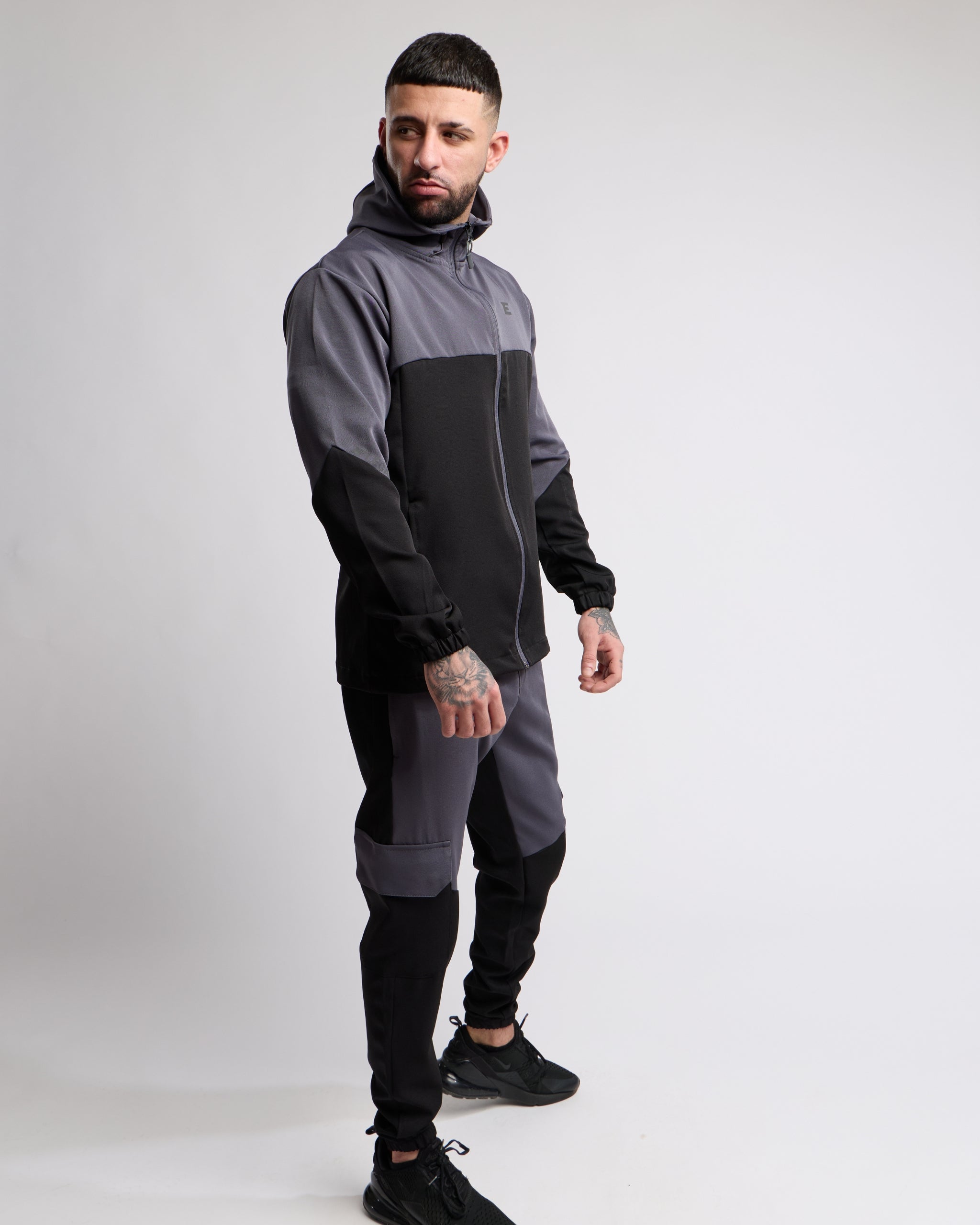 Man wearing a black and gray sports tracksuit jacket with matching tracksuit pants on a white background