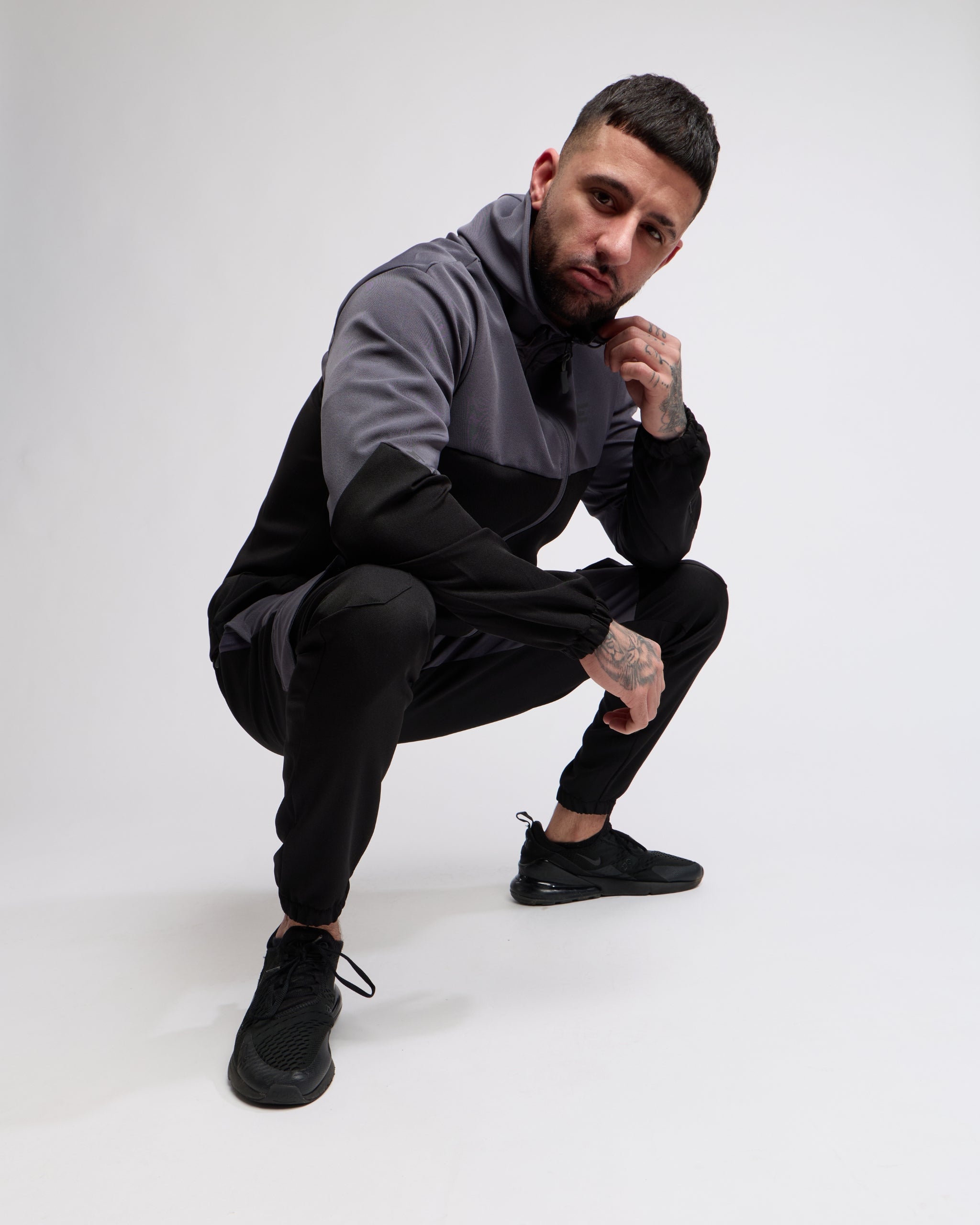 Man wearing a black and gray sports tracksuit jacket with matching tracksuit pants on a white background