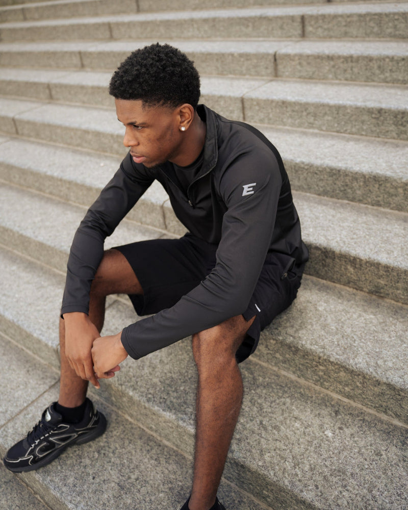 man sitting on steps wearing a black athletic outfit with a logo.
