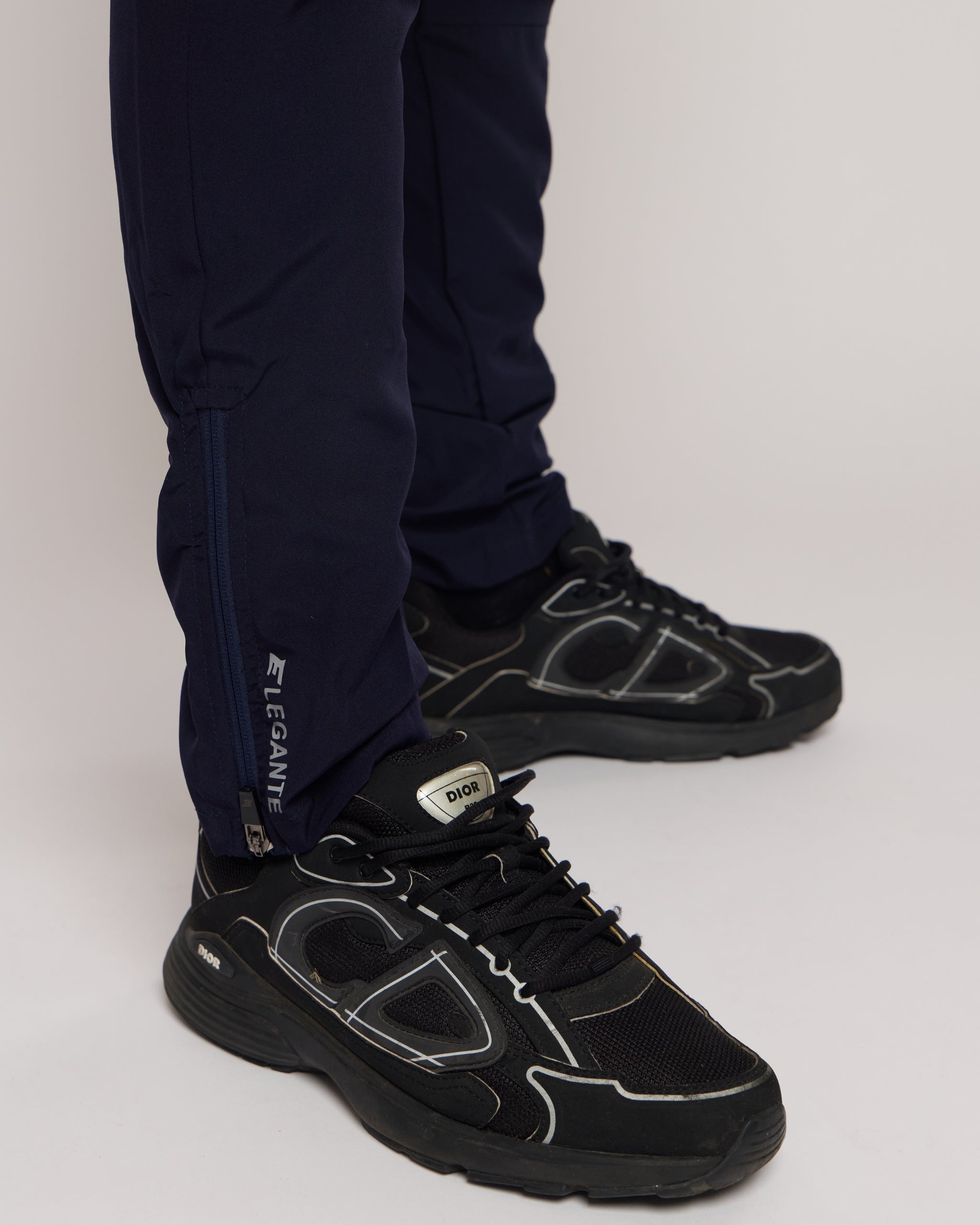 Black athletic shoes worn with navy pants on a light gray background