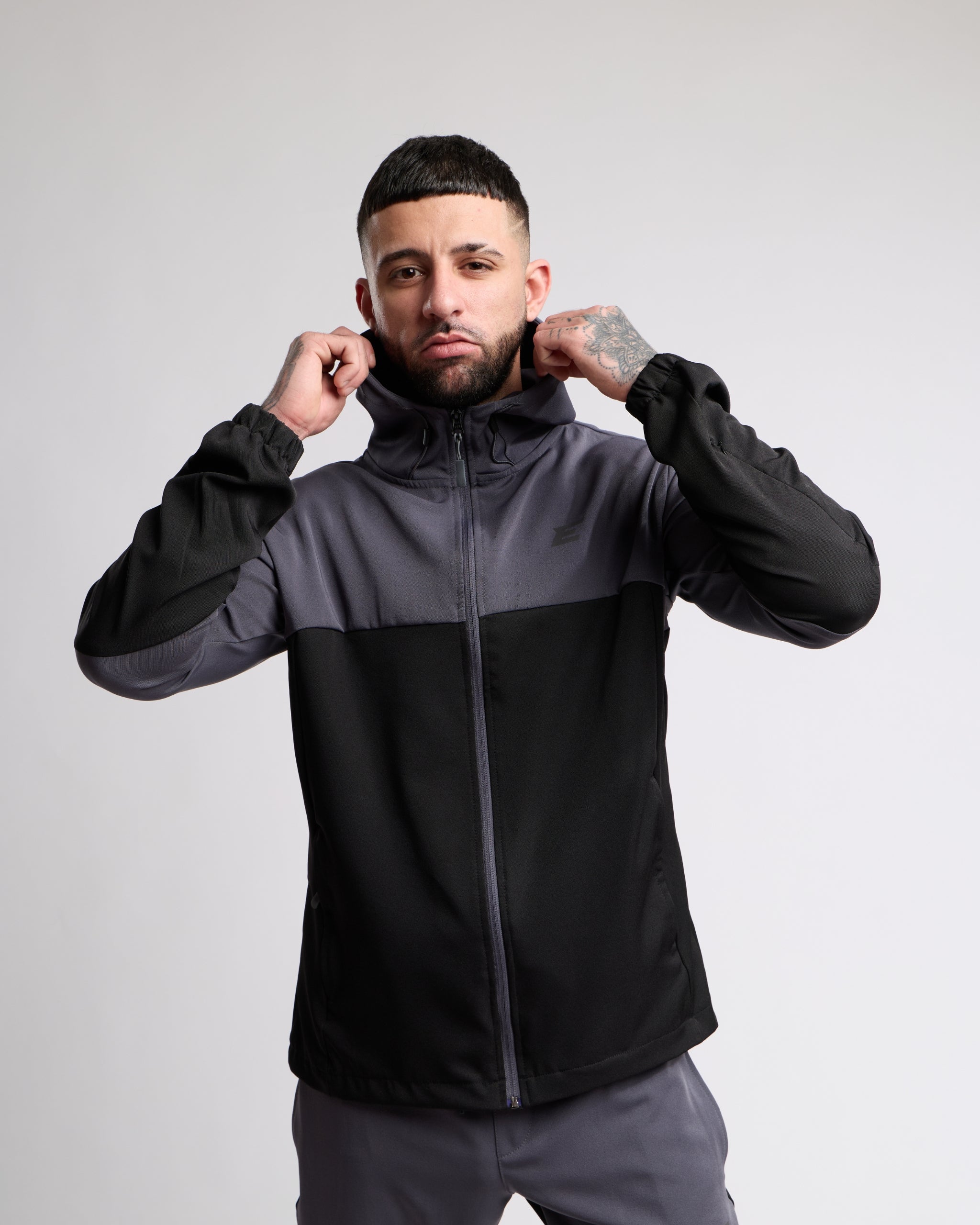 Man wearing a black and gray sports tracksuit jacket with hood and matching tracksuit pants on a white background