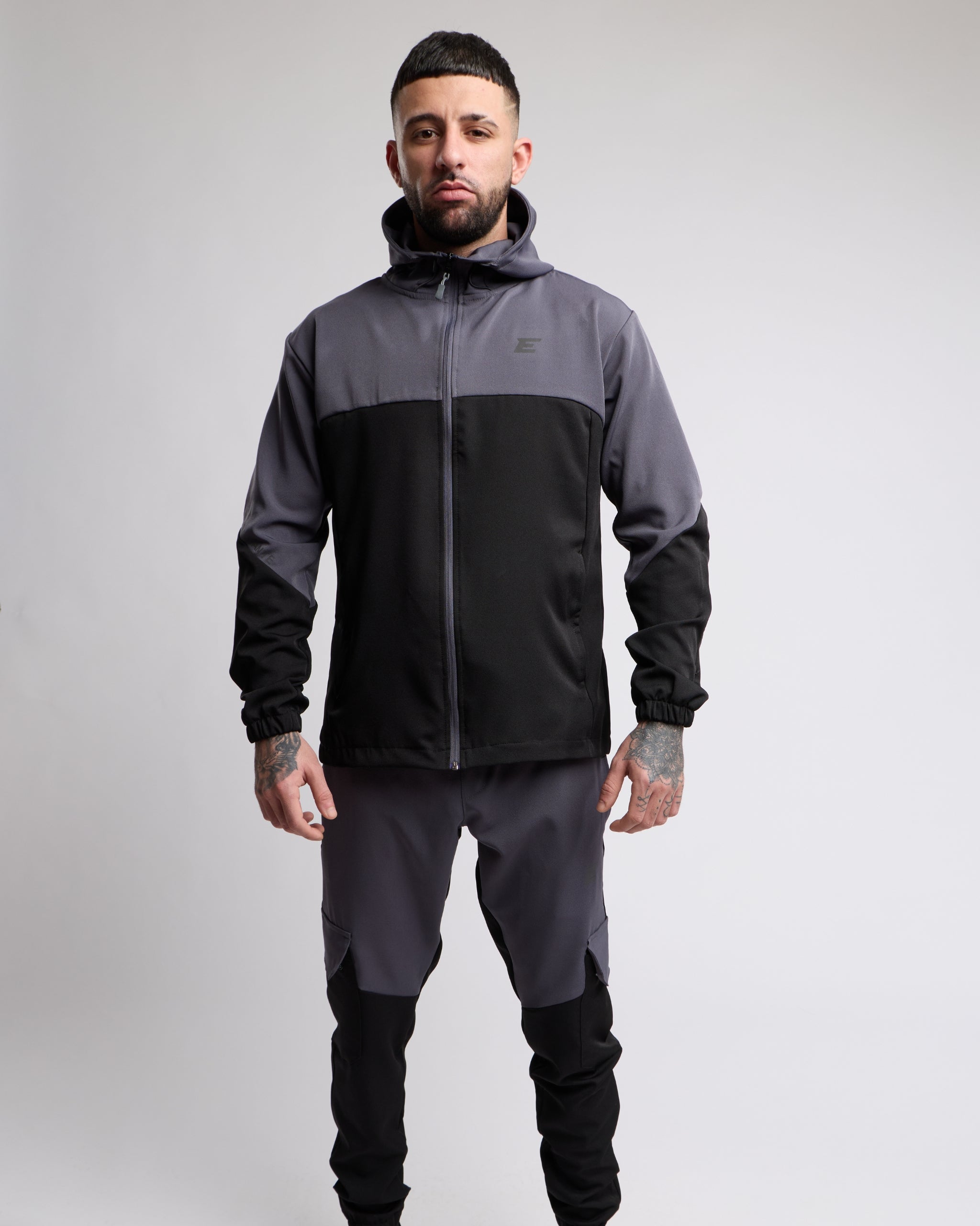 Man wearing a black and gray sports tracksuit jacket with matching tracksuit pants on a white background
