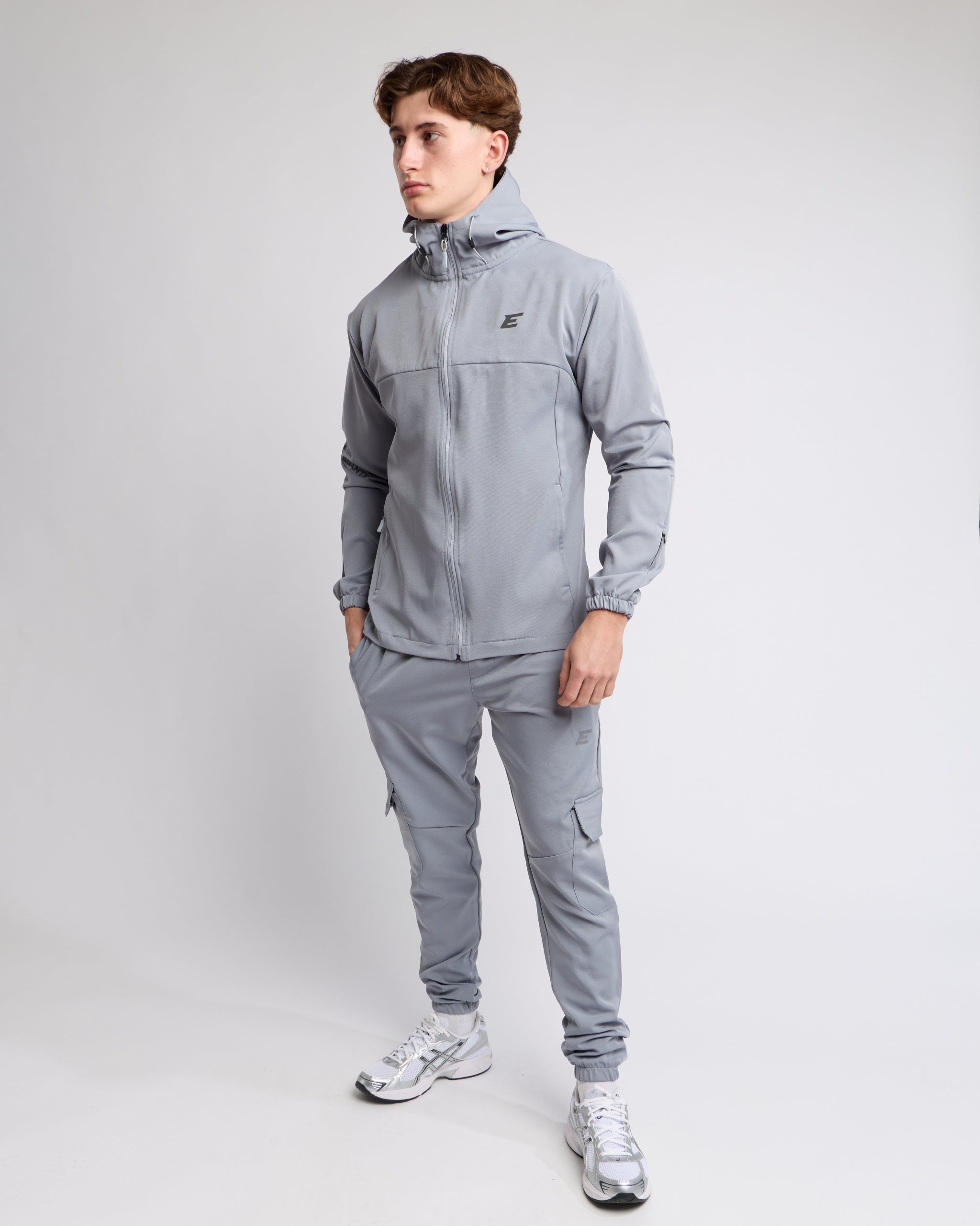 Man wearing an all grey sports tracksuit jacket with hood and trousers on a white background