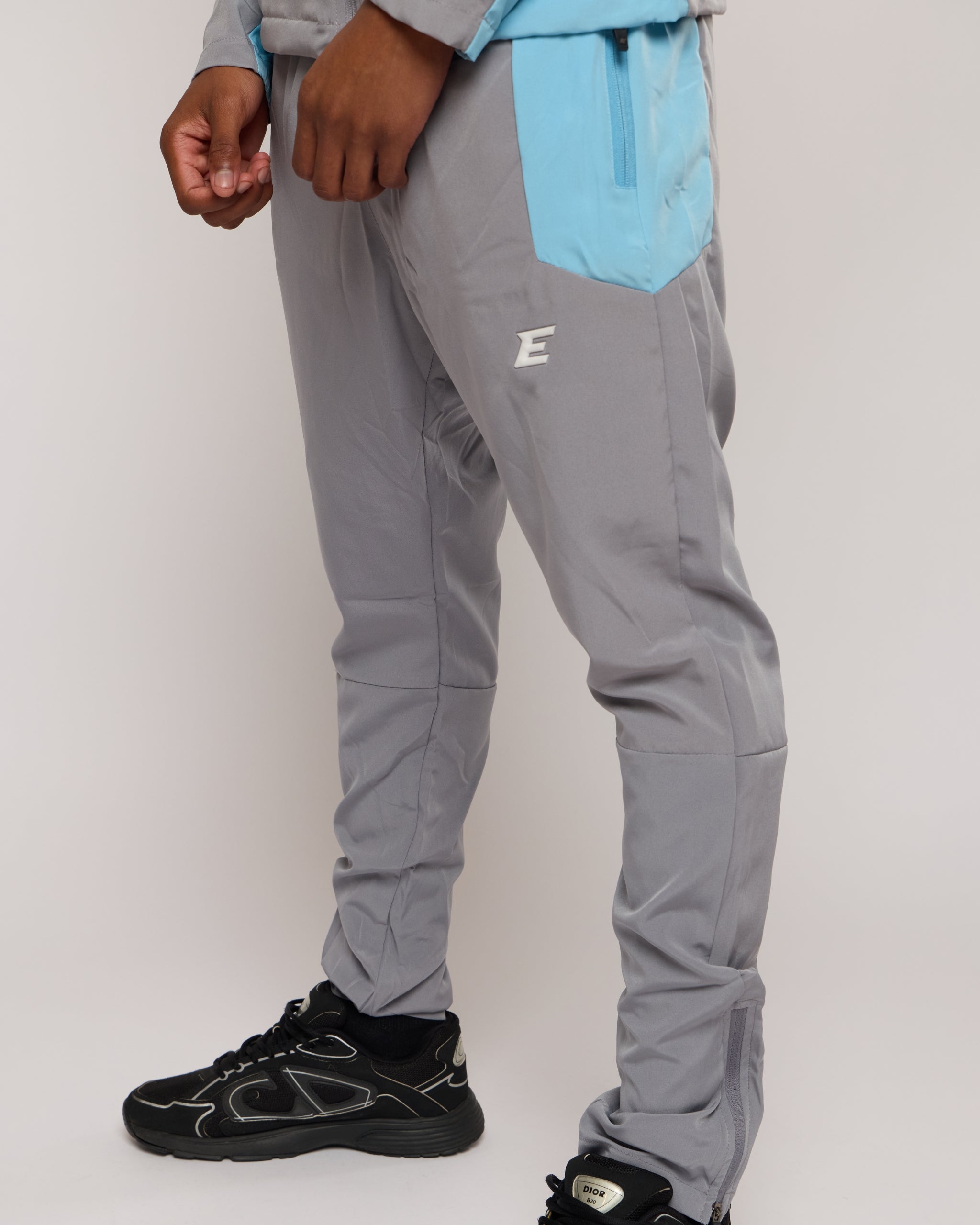 Man wearing a grey and blue tracksuit joggers with an E logo on a plain background