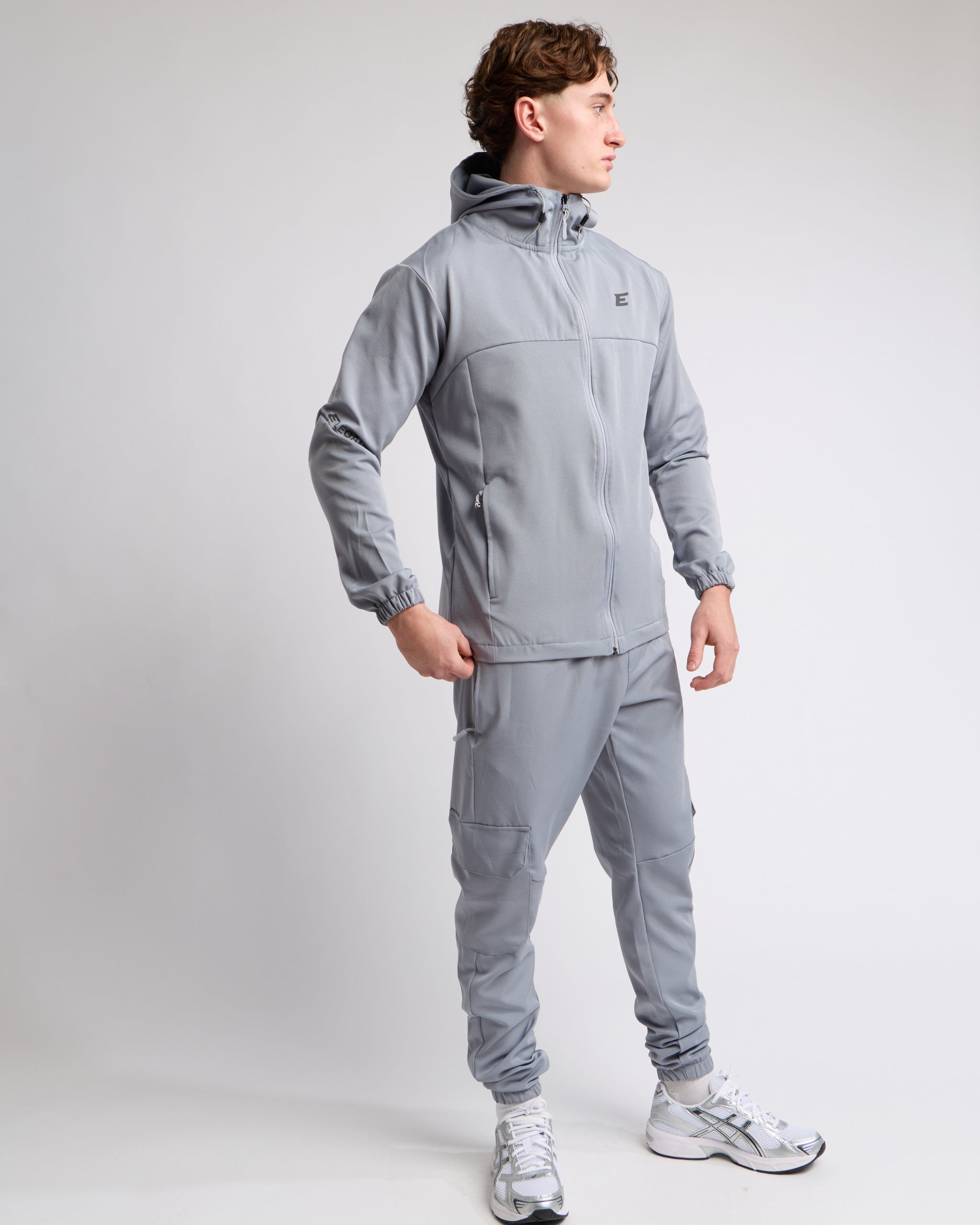 Man wearing an all grey sports tracksuit jacket with hood and trousers on a white background