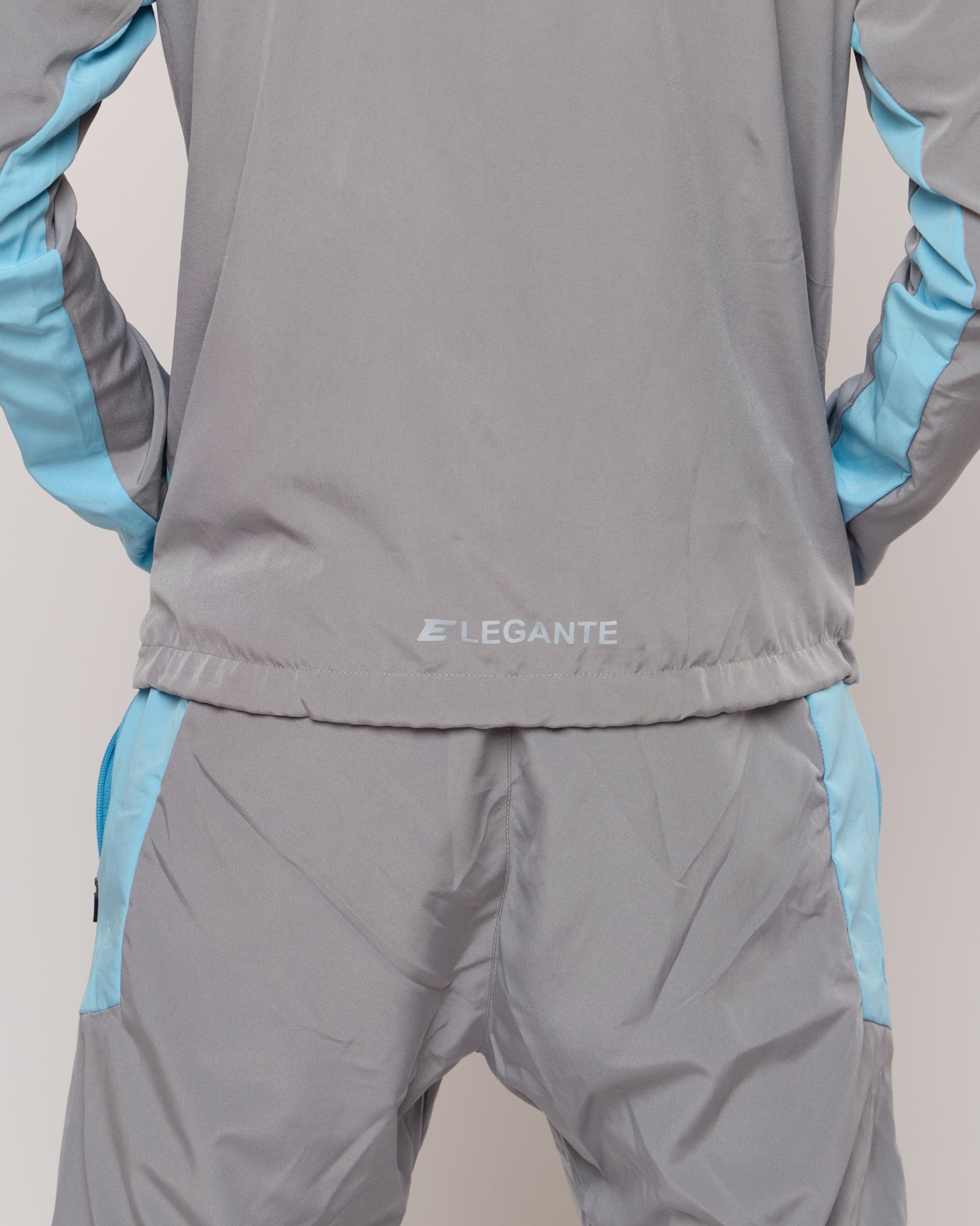 Man wearing a grey and blue tracksuit jacket with zip pockets with an Elegante logo on a plain background