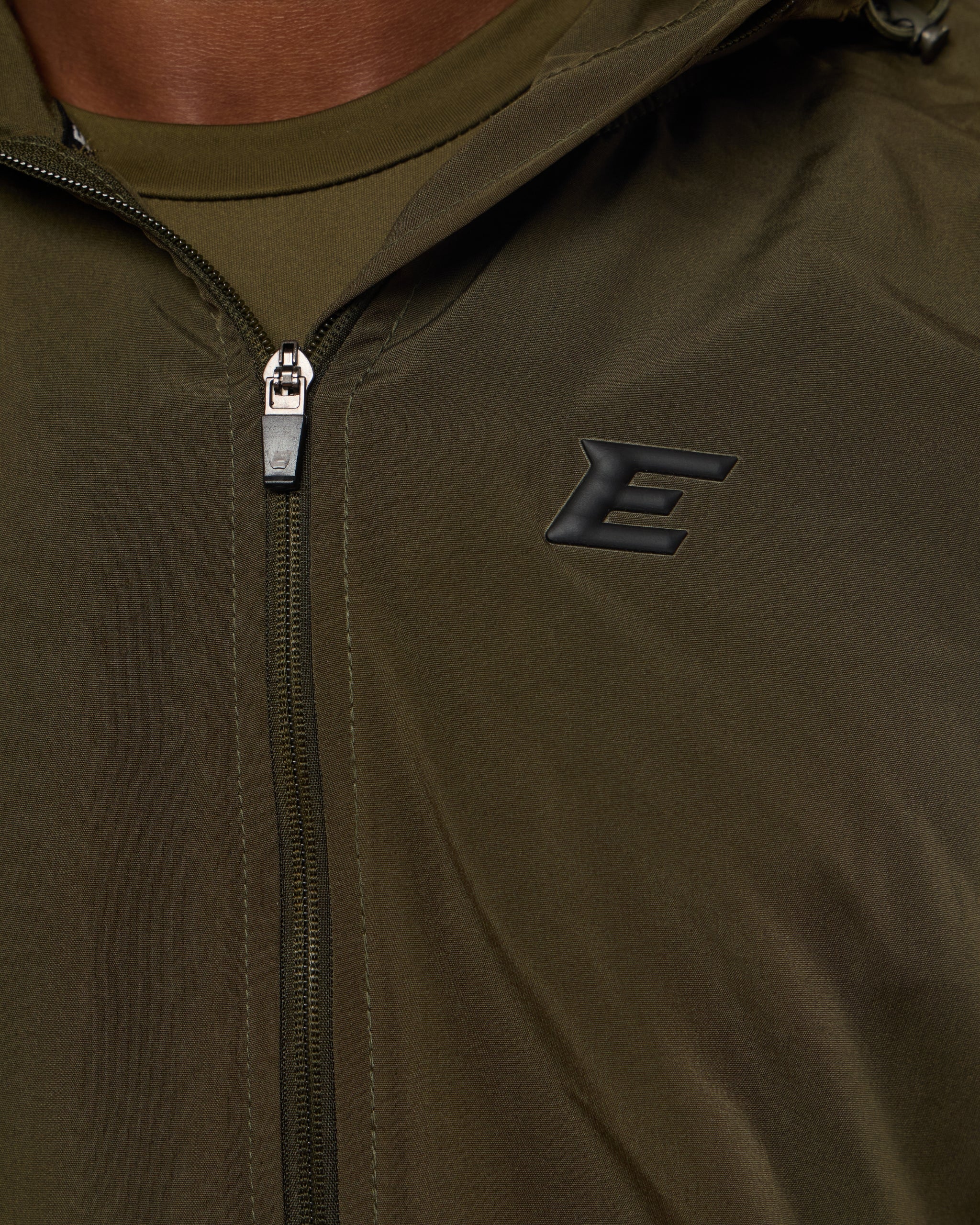 Close-up of a green jacket with a zipper and a logo on the chest.
