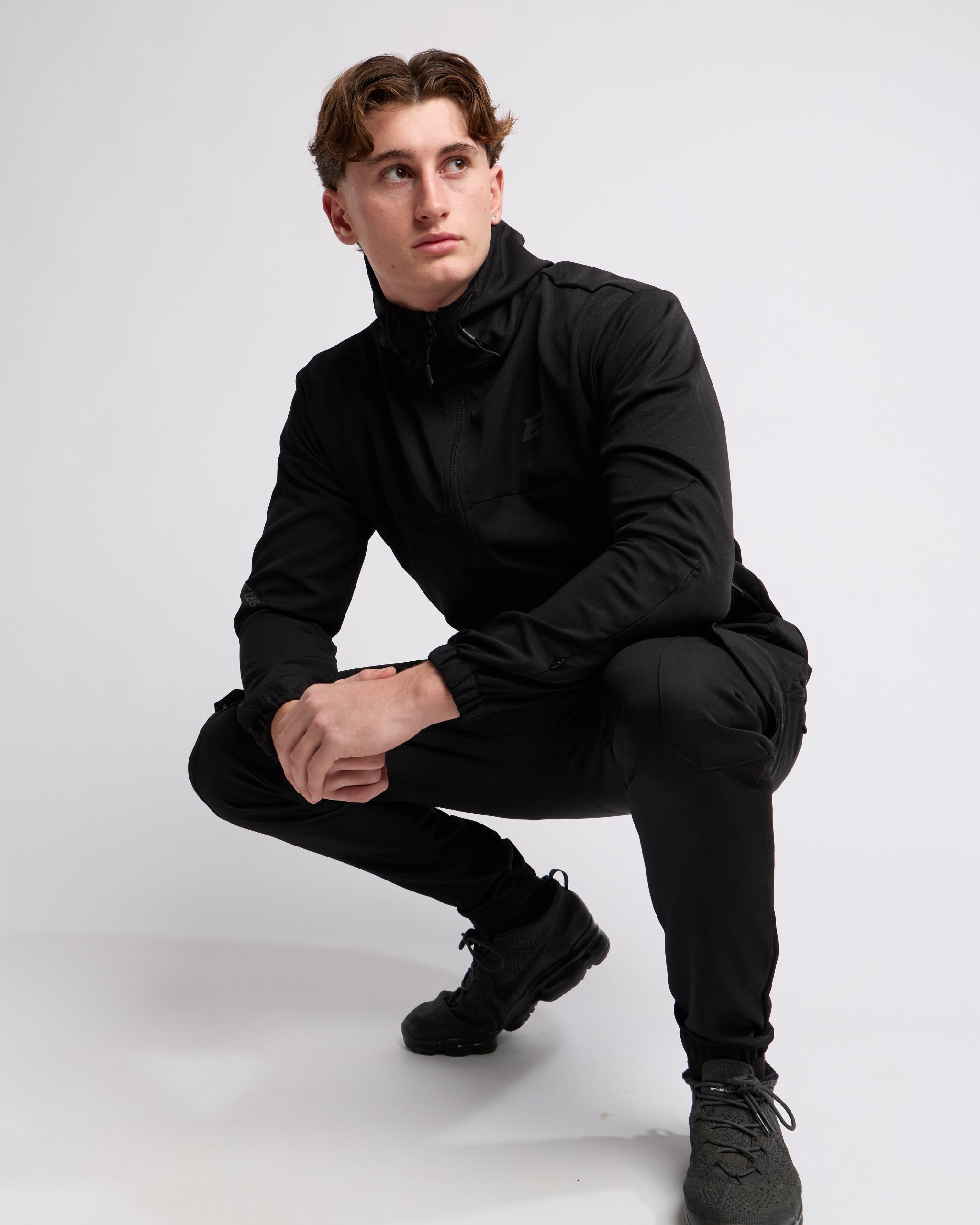 Man wearing an all Black sports tracksuit jacket and trousers on a white background