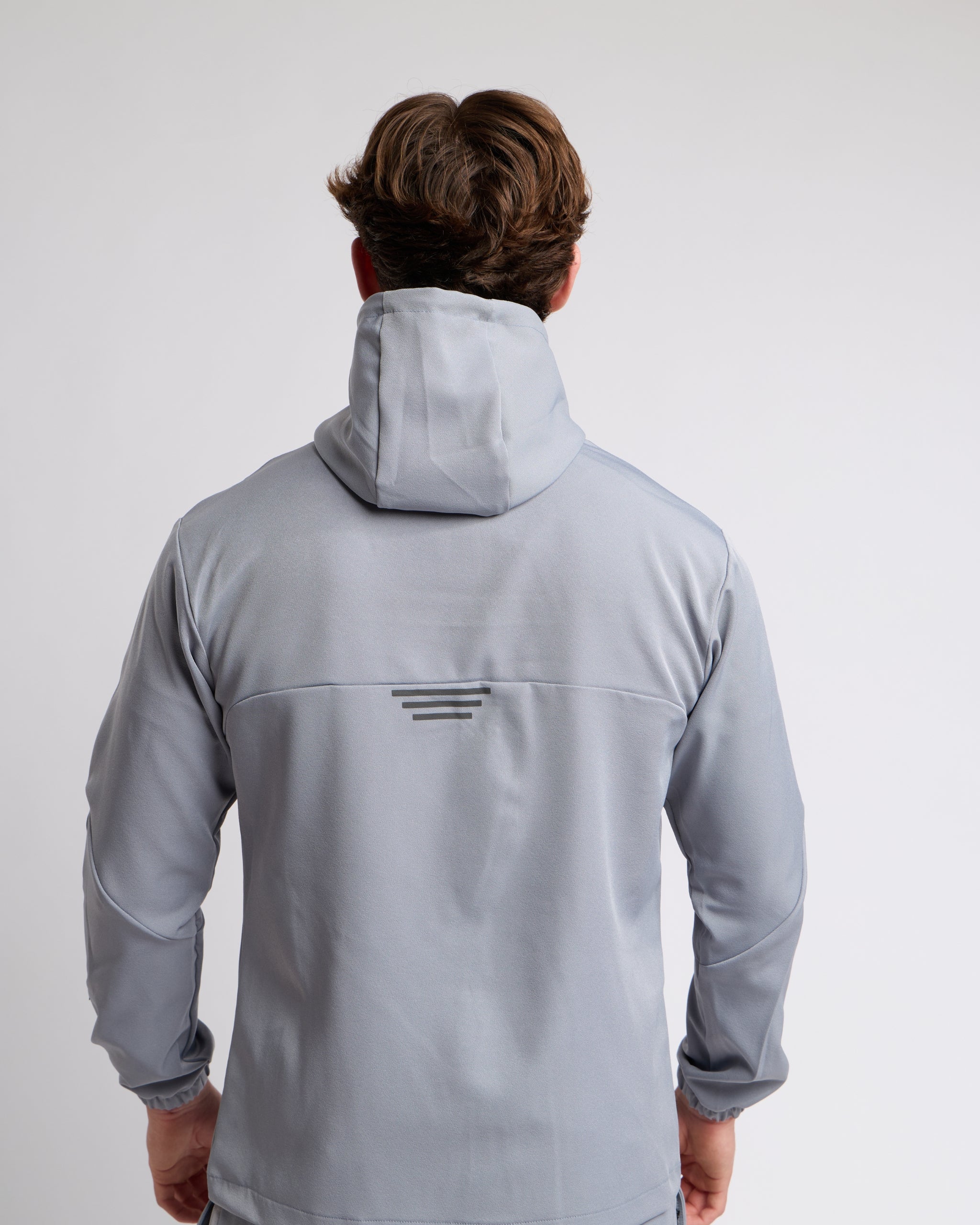 Man wearing a gray jacket with hood and reflective ascent on a light gray background