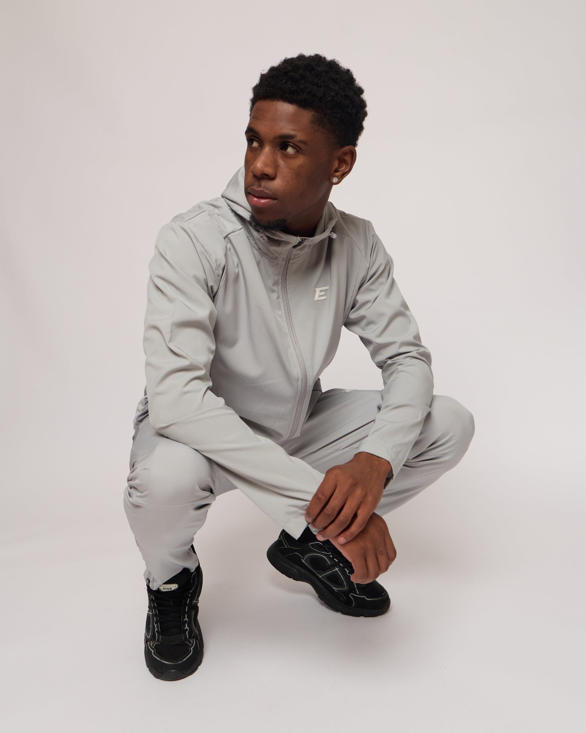 Man wearing a light gray jacket with a hood and matching joggers on a plain background