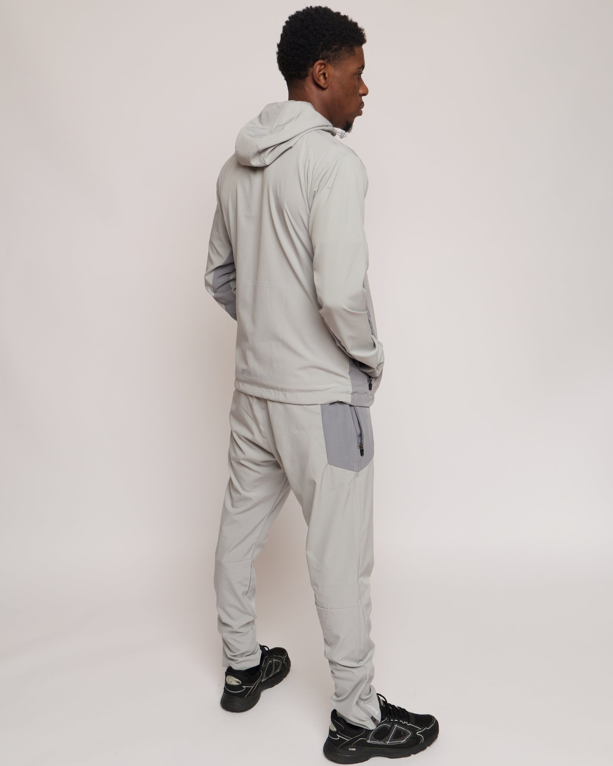 Man wearing a light gray jacket with a hood and matching joggers on a plain background