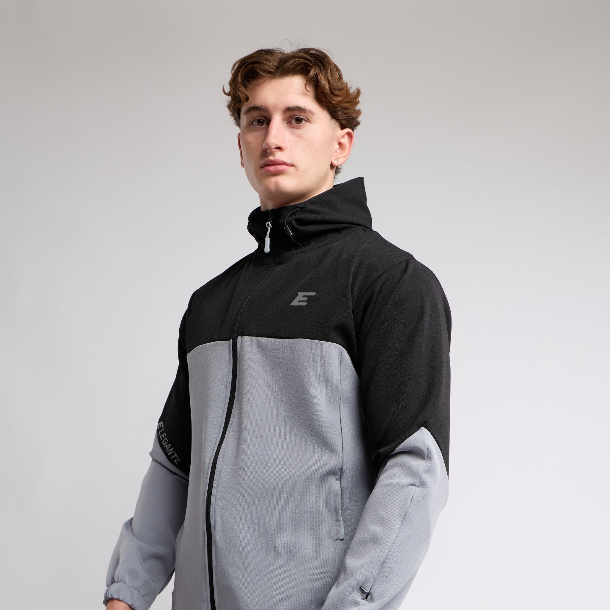 man wearing a black and gray jacket with a brand logo on a light gray background