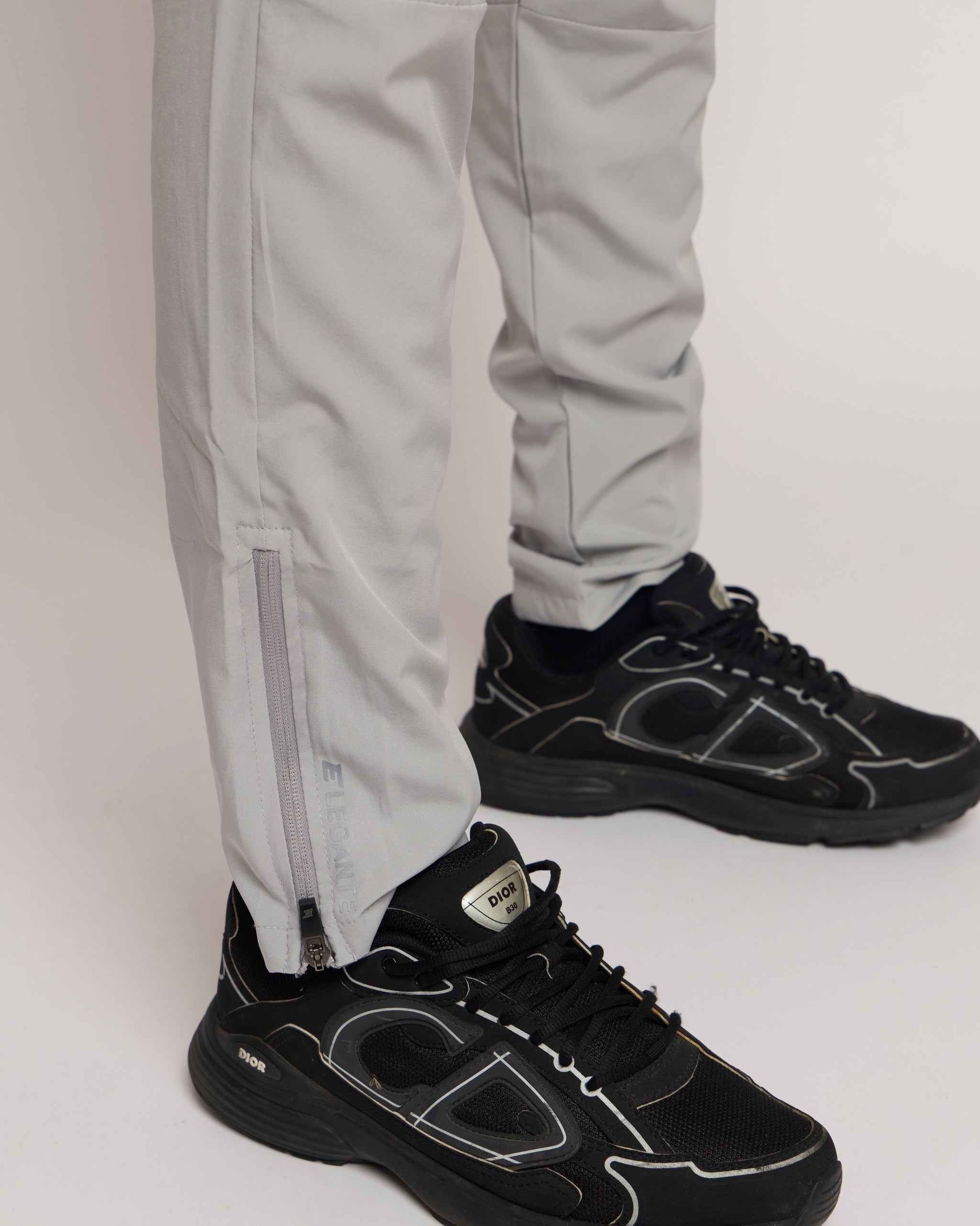 man wearing grey tracksuit joggers, black sneakers with a white background