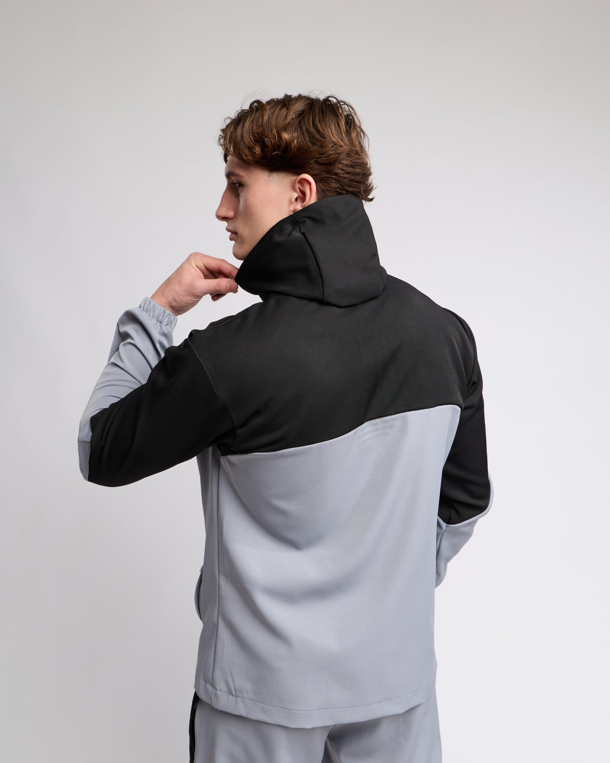 man wearing a black and gray tracksuit with hood on a light gray background