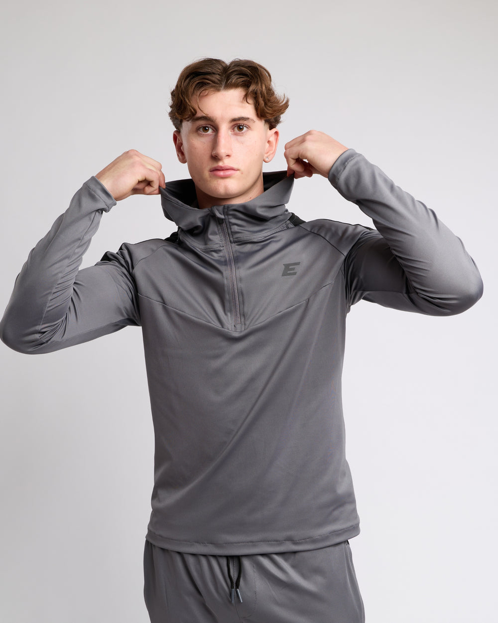 Man wearing a gray athletic outfit with a brand logo on a light gray background