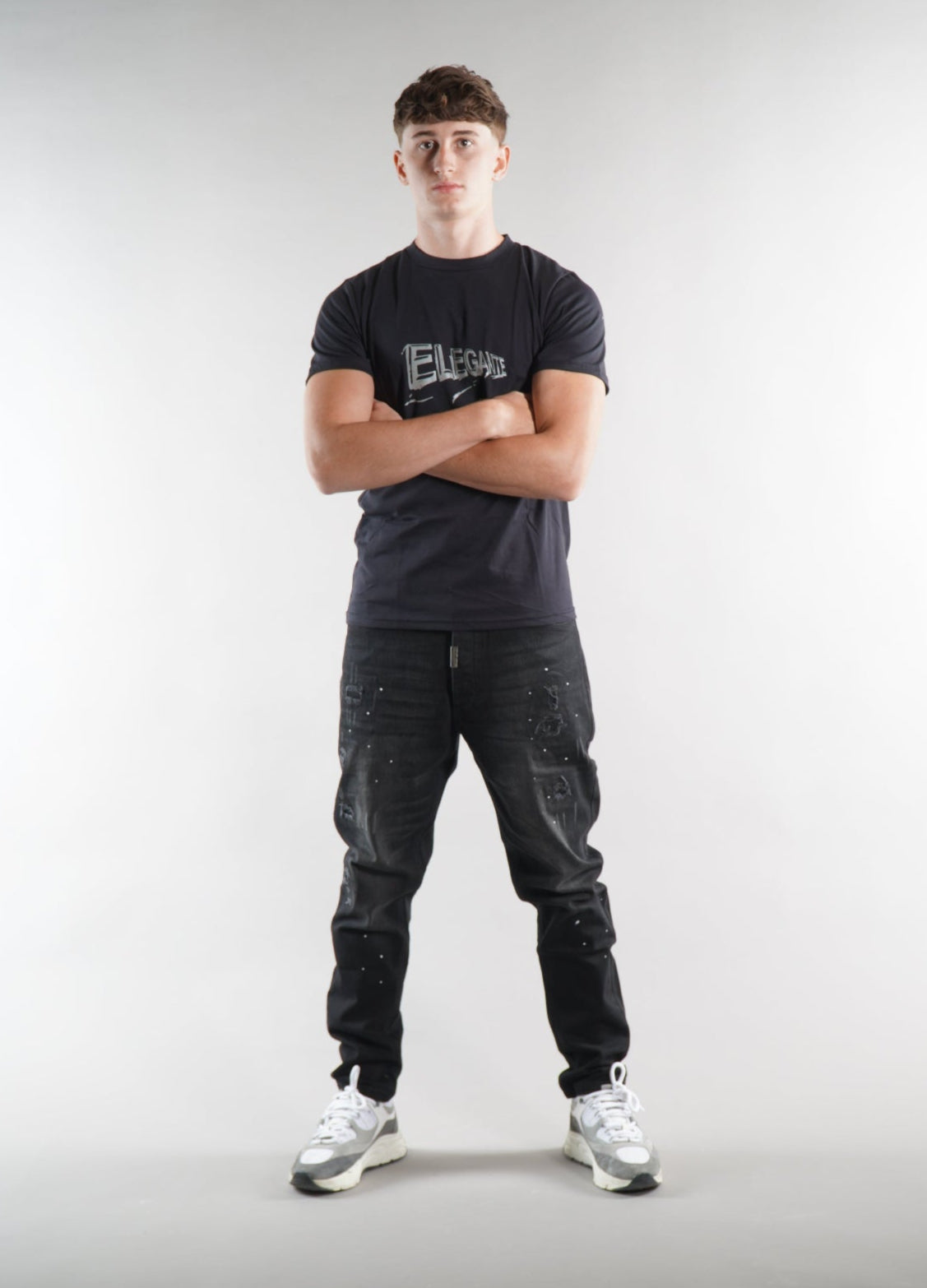 man wearing Elegante logo T-Shirt in black with black denim jeans on white background
