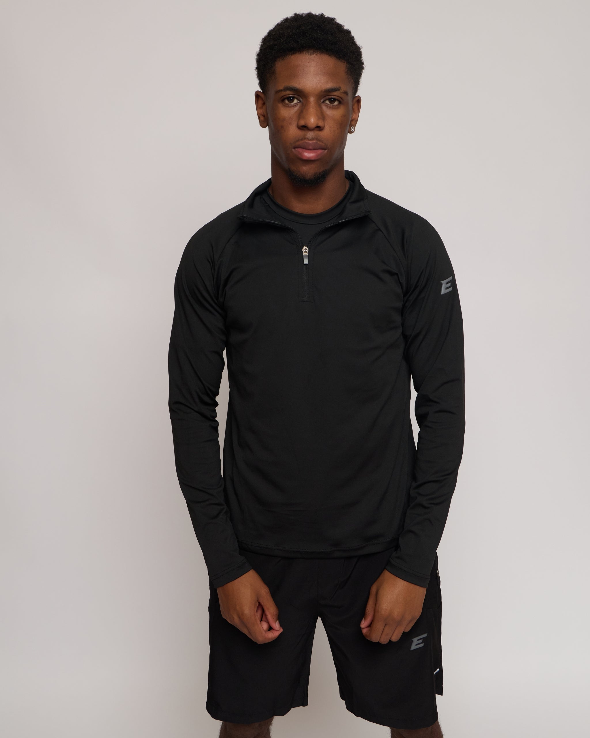 Man wearing a long sleeve black athletic quarter zip top with a white 'E' logo with matching shorts on a light background